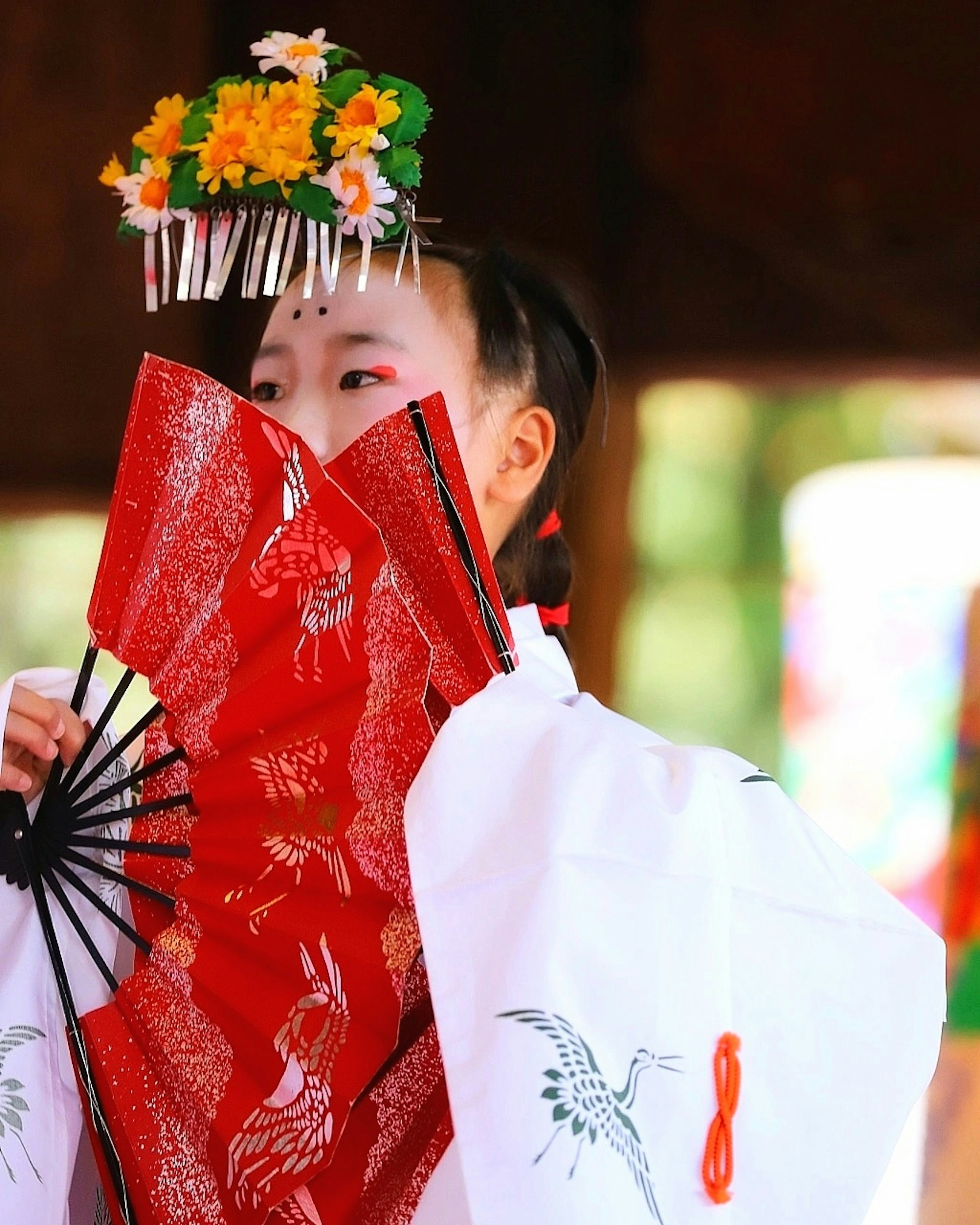 Donna in kimono tradizionale che tiene un ventaglio rosso con un copricapo floreale