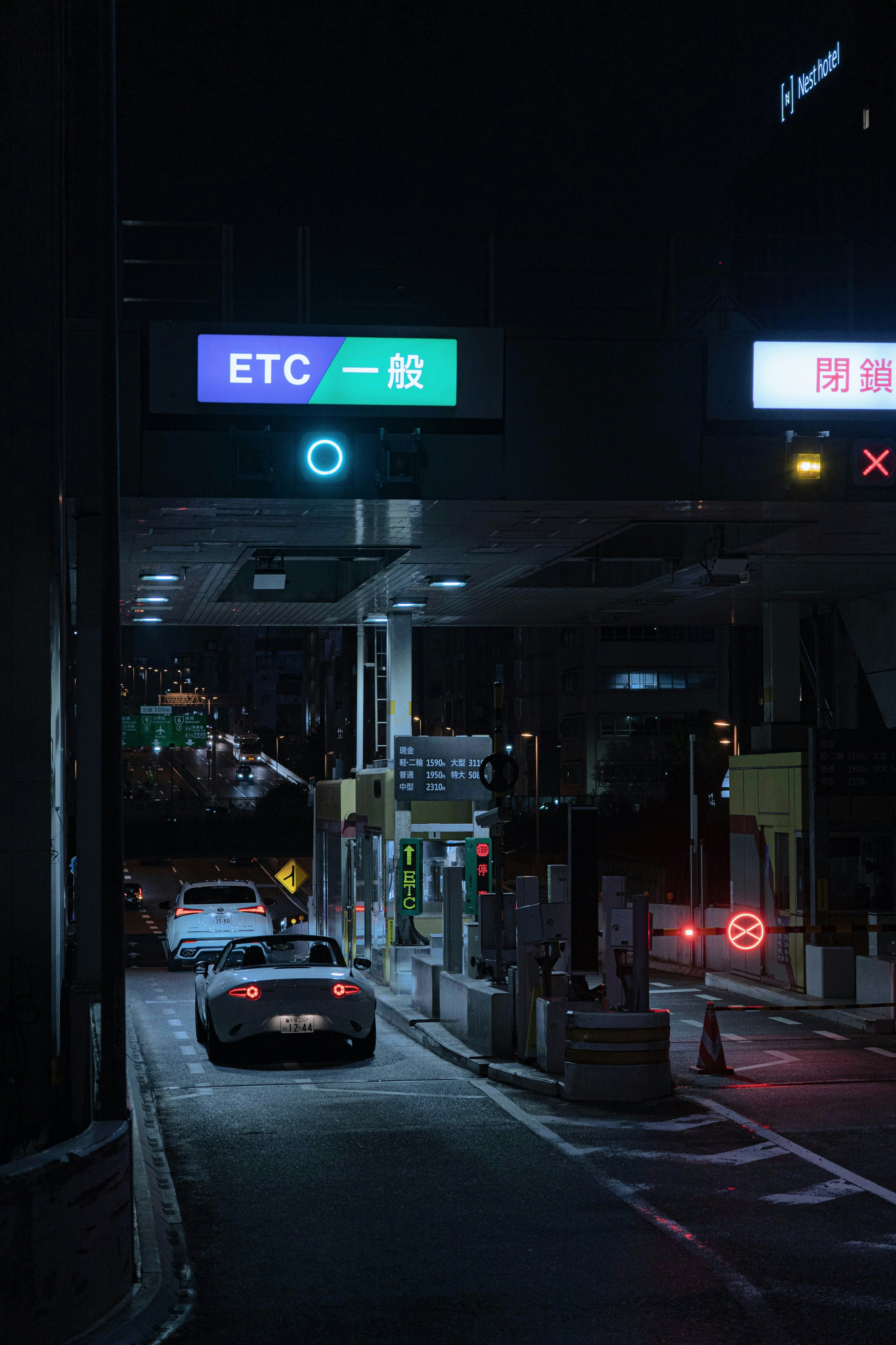 Scène nocturne d'un péage avec une voiture passant sous un panneau ETC lumineux