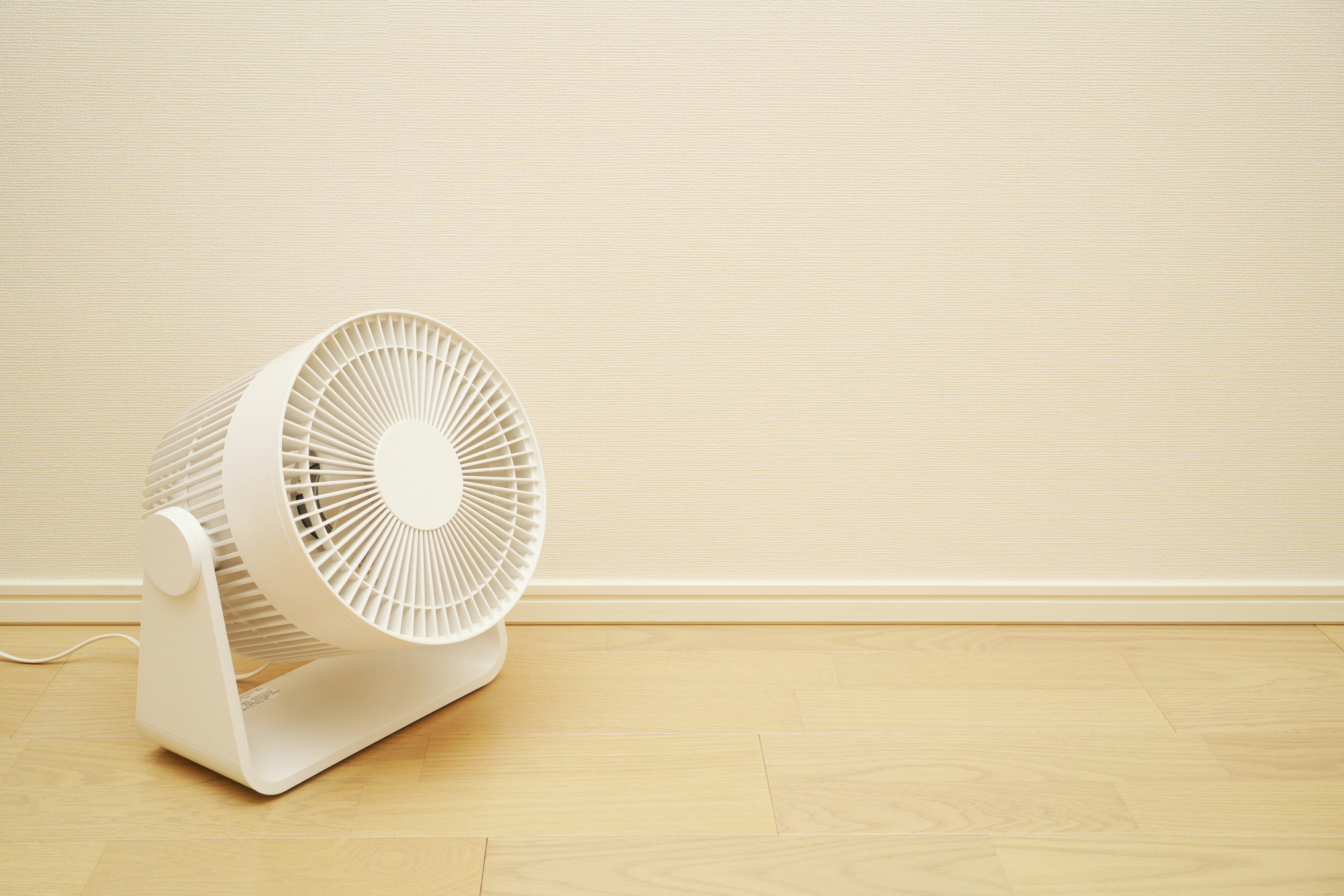 Un ventilatore bianco posizionato nell'angolo di una stanza con uno sfondo minimalista