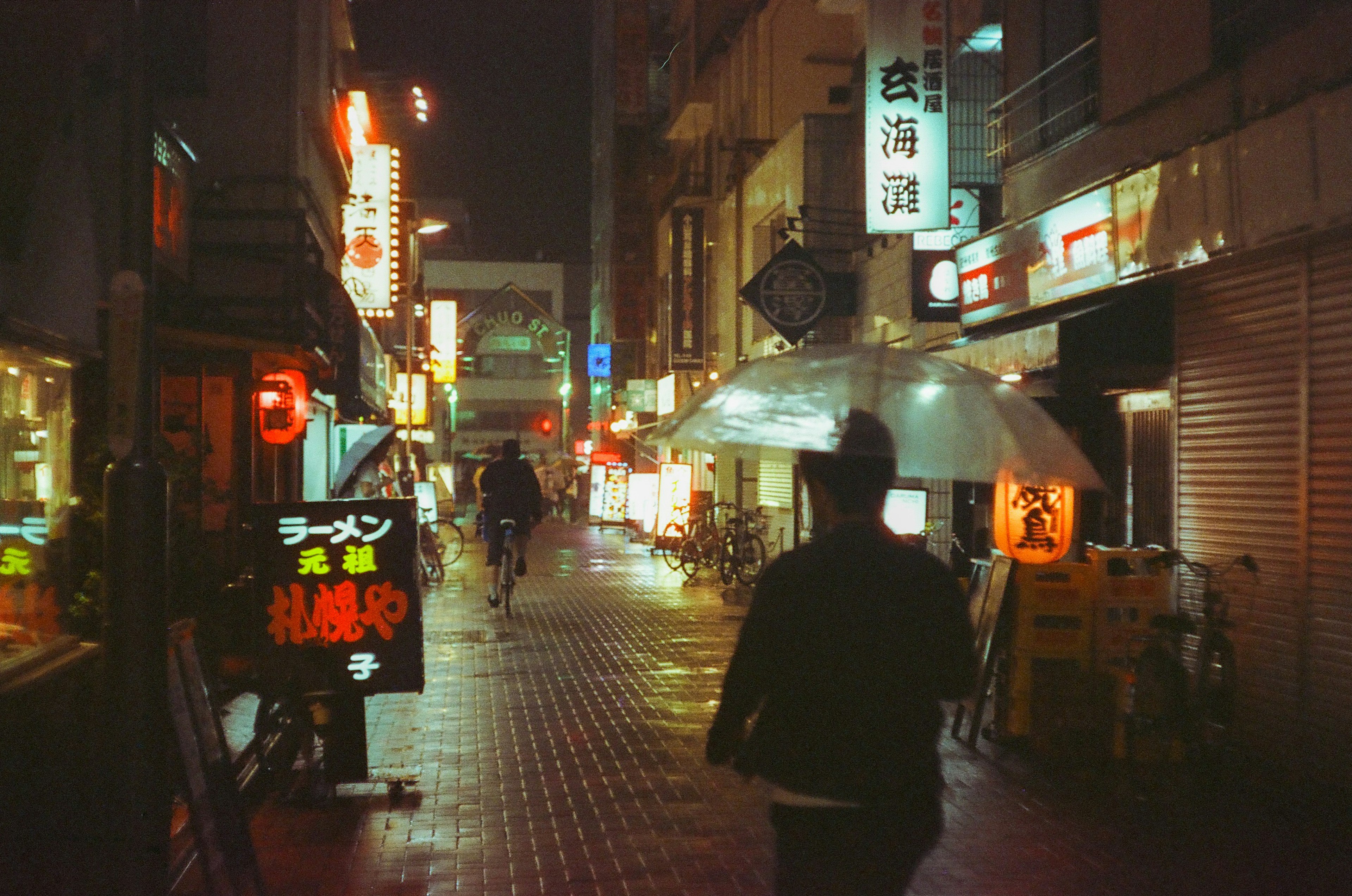 夜の街並みに傘を差した人が歩いている風景