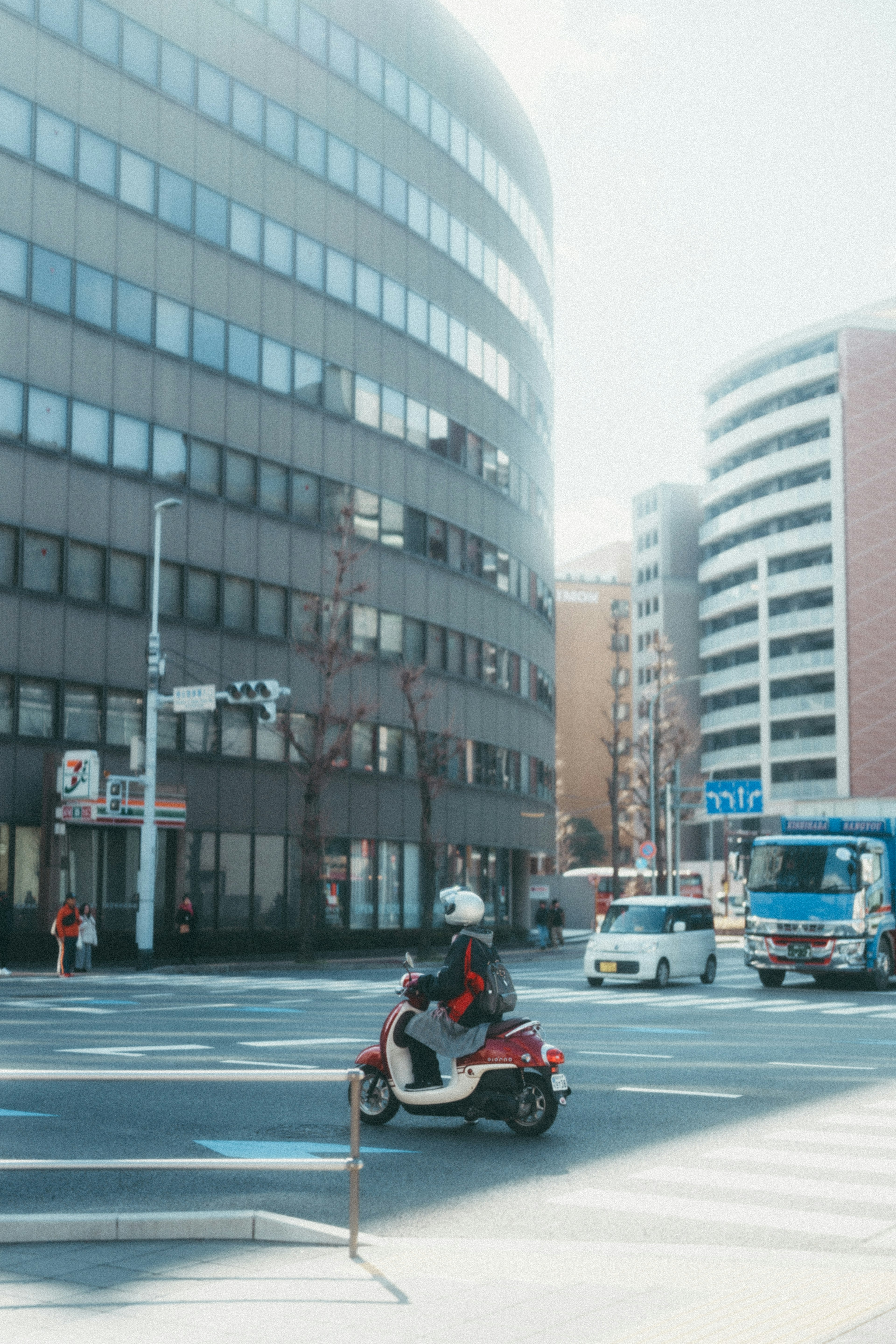 Delivery rider on a scooter at an urban intersection with modern buildings