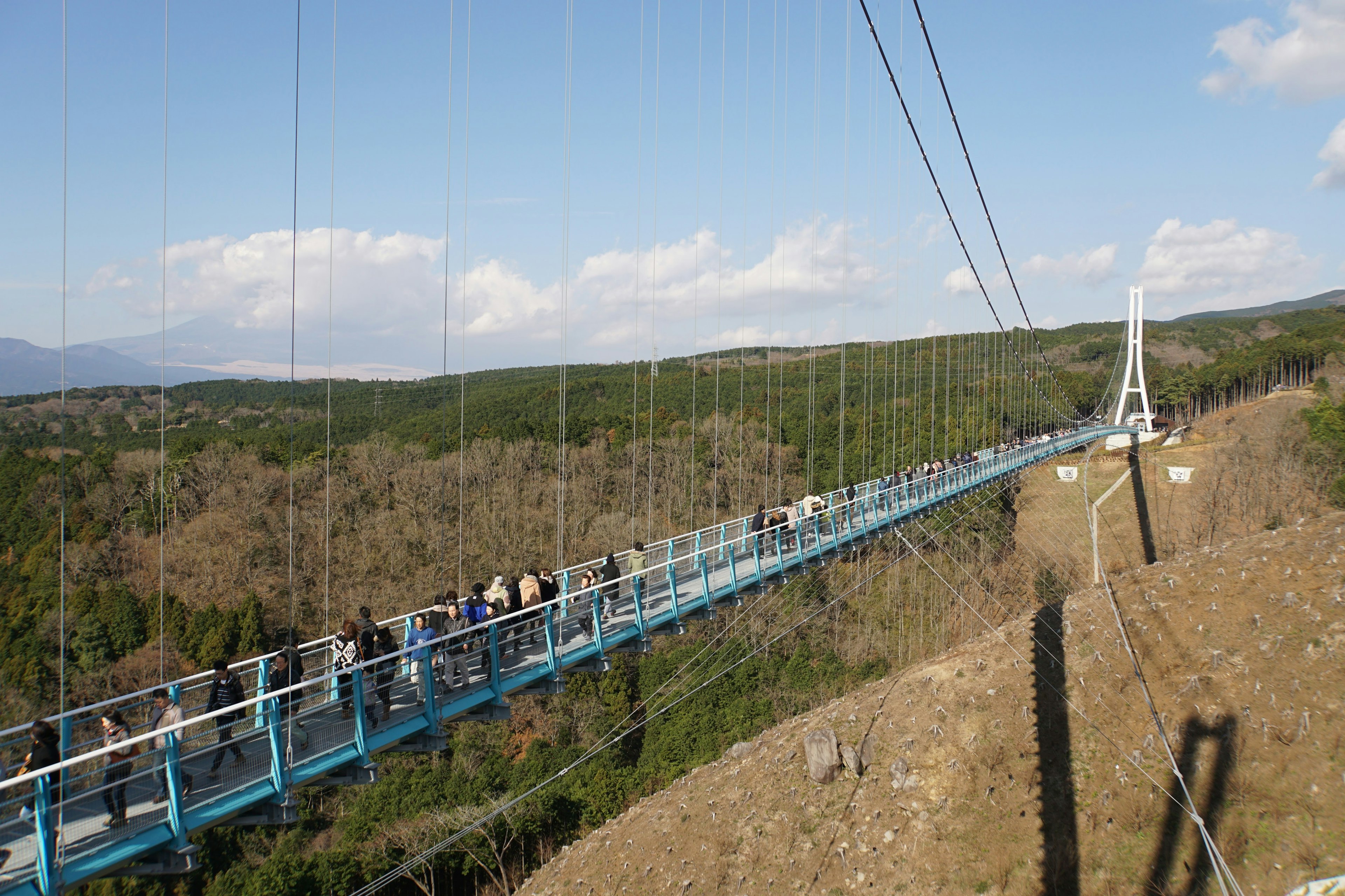 Eine lange Hängebrücke mit Menschen, die sie überqueren, und grünen Bergen im Hintergrund