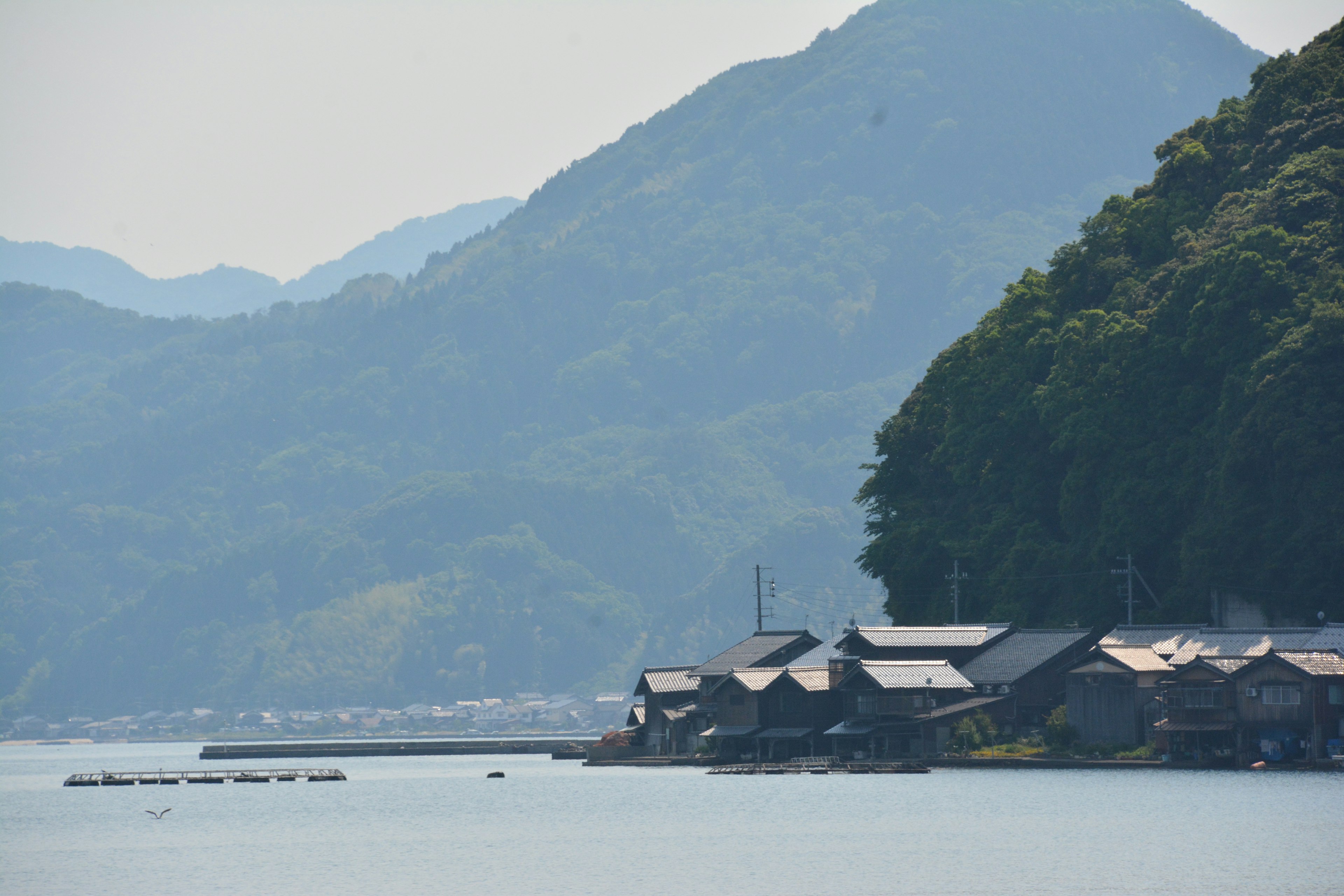 Malersicher Blick auf traditionelle japanische Häuser entlang eines ruhigen Meeres mit Bergen im Hintergrund