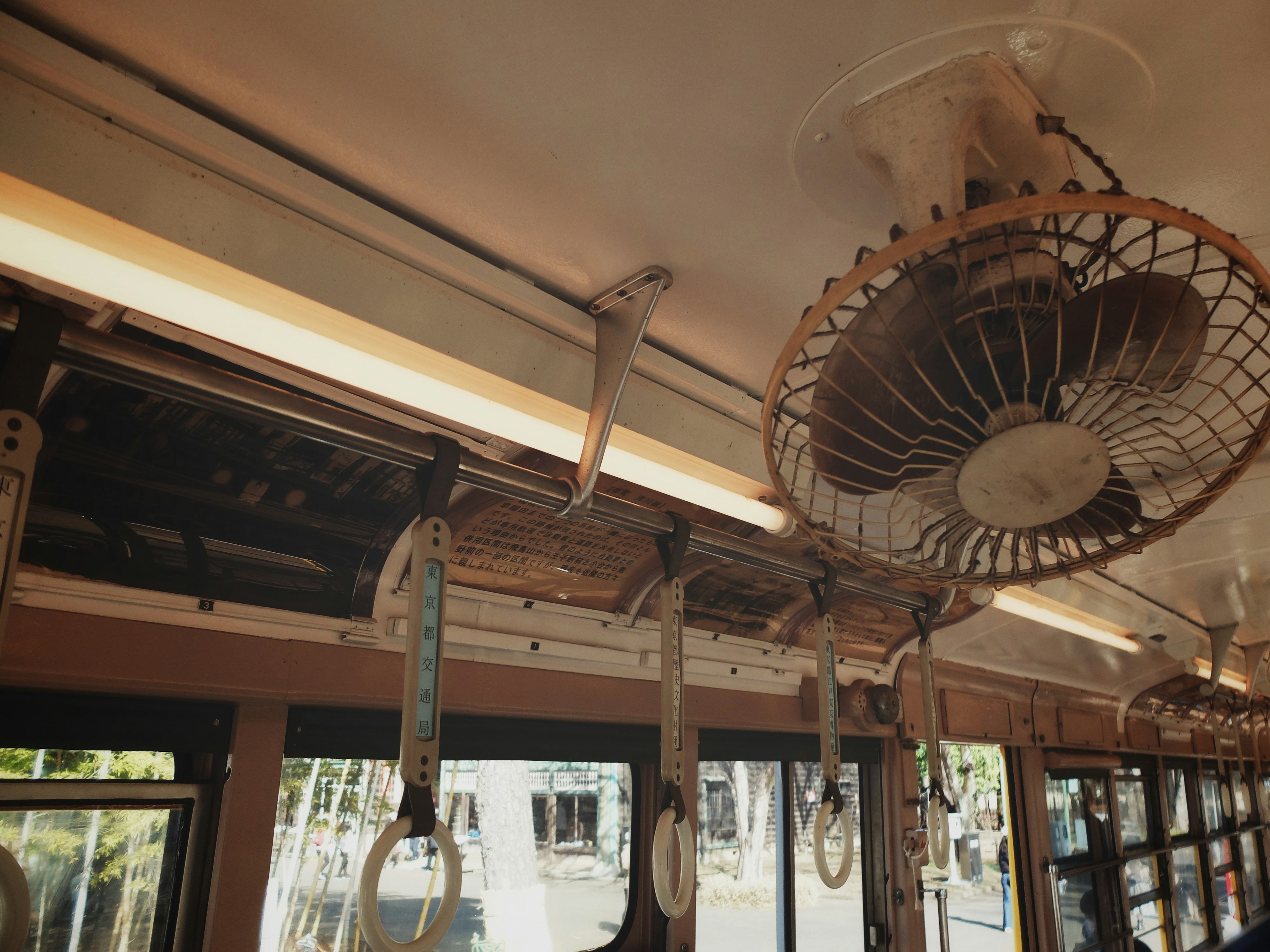 Interior view of a train with a ceiling fan and hanging straps