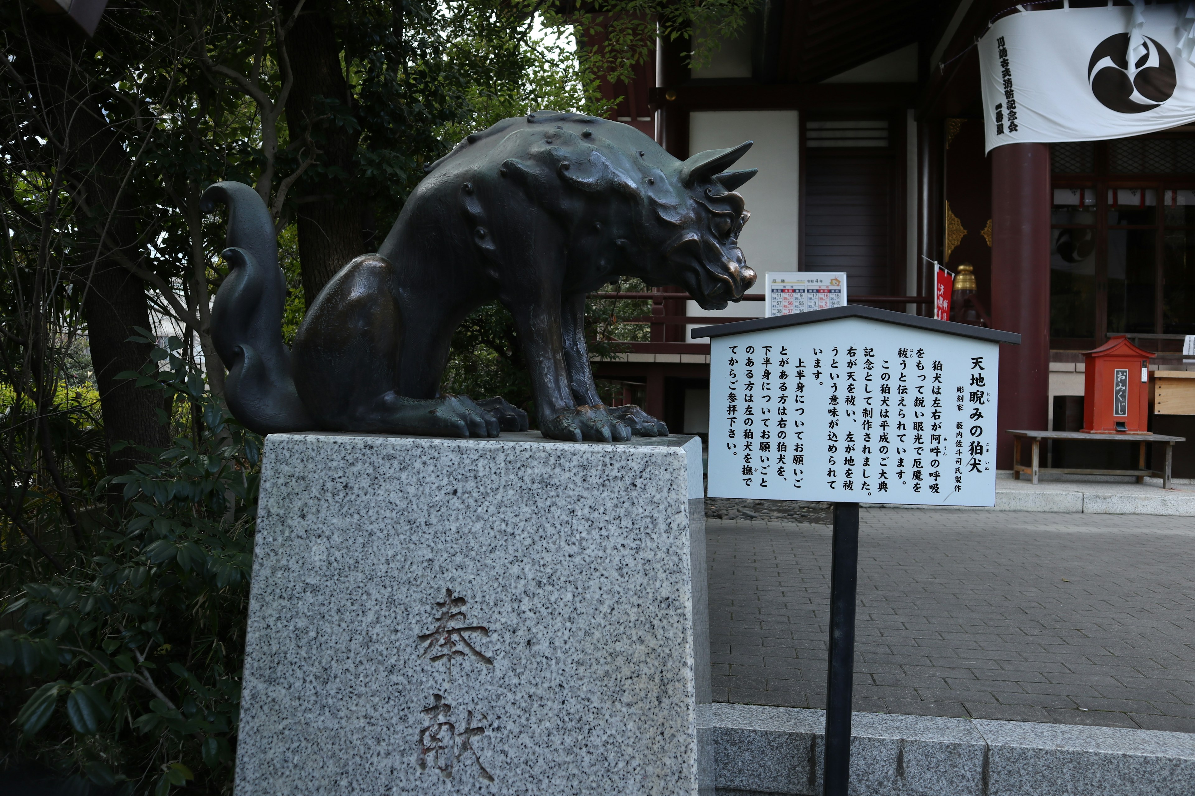 Eine schwarze Statue eines Wächterhundes vor einem Schrein mit einer Informationstafel