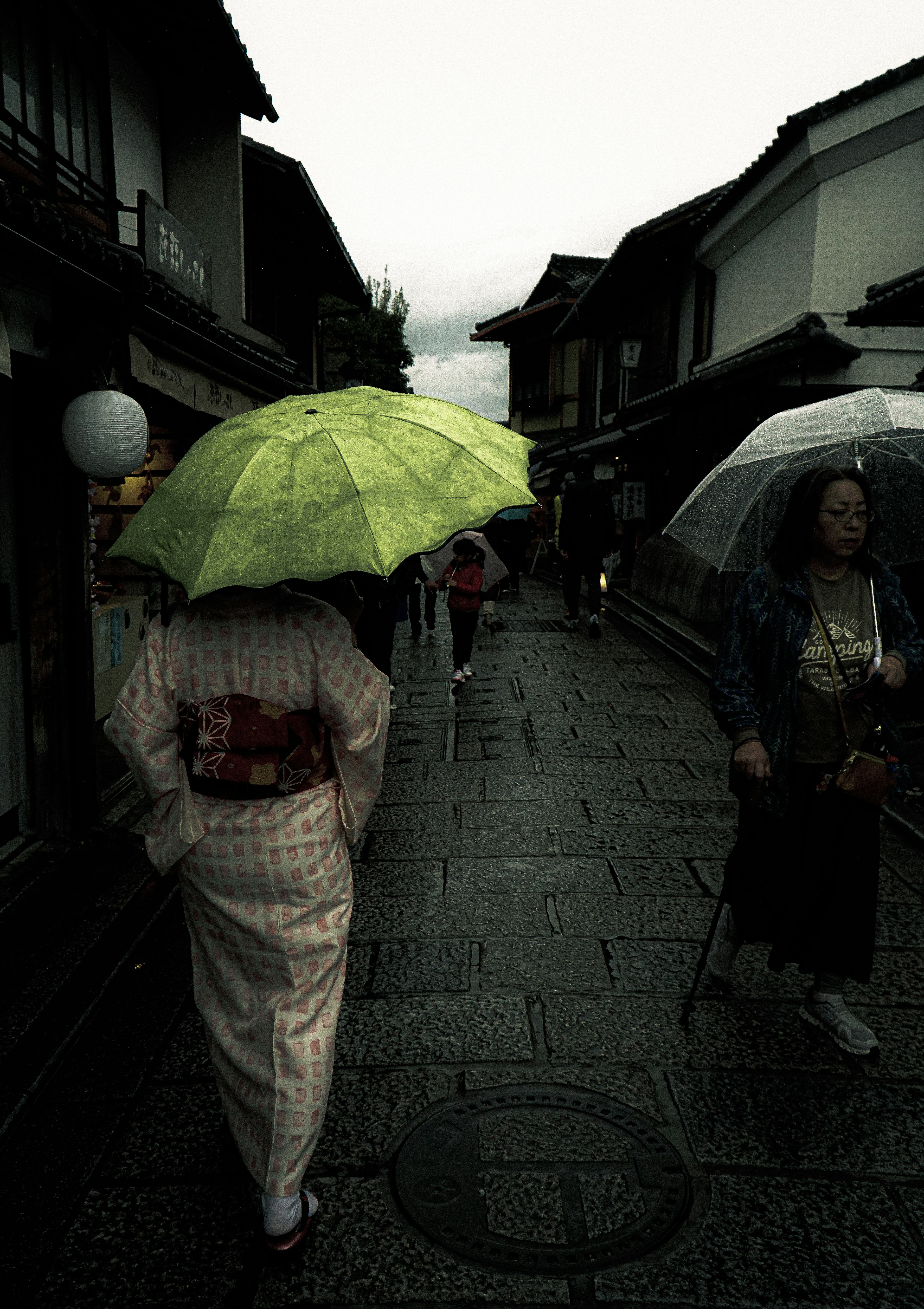 雨の中を歩く着物を着た女性が緑の傘を持っている街並み