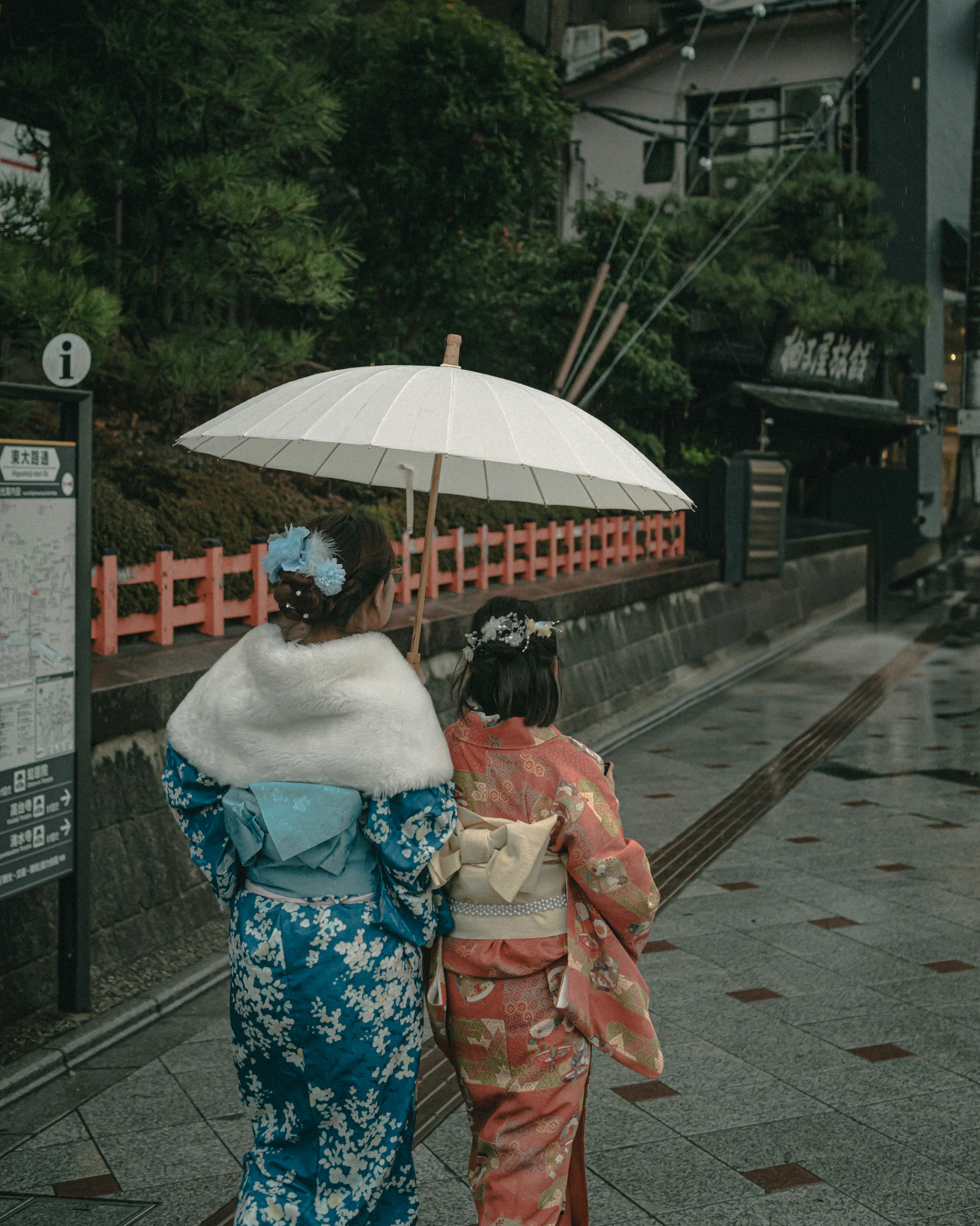 Two women wearing kimonos holding an umbrella walking together