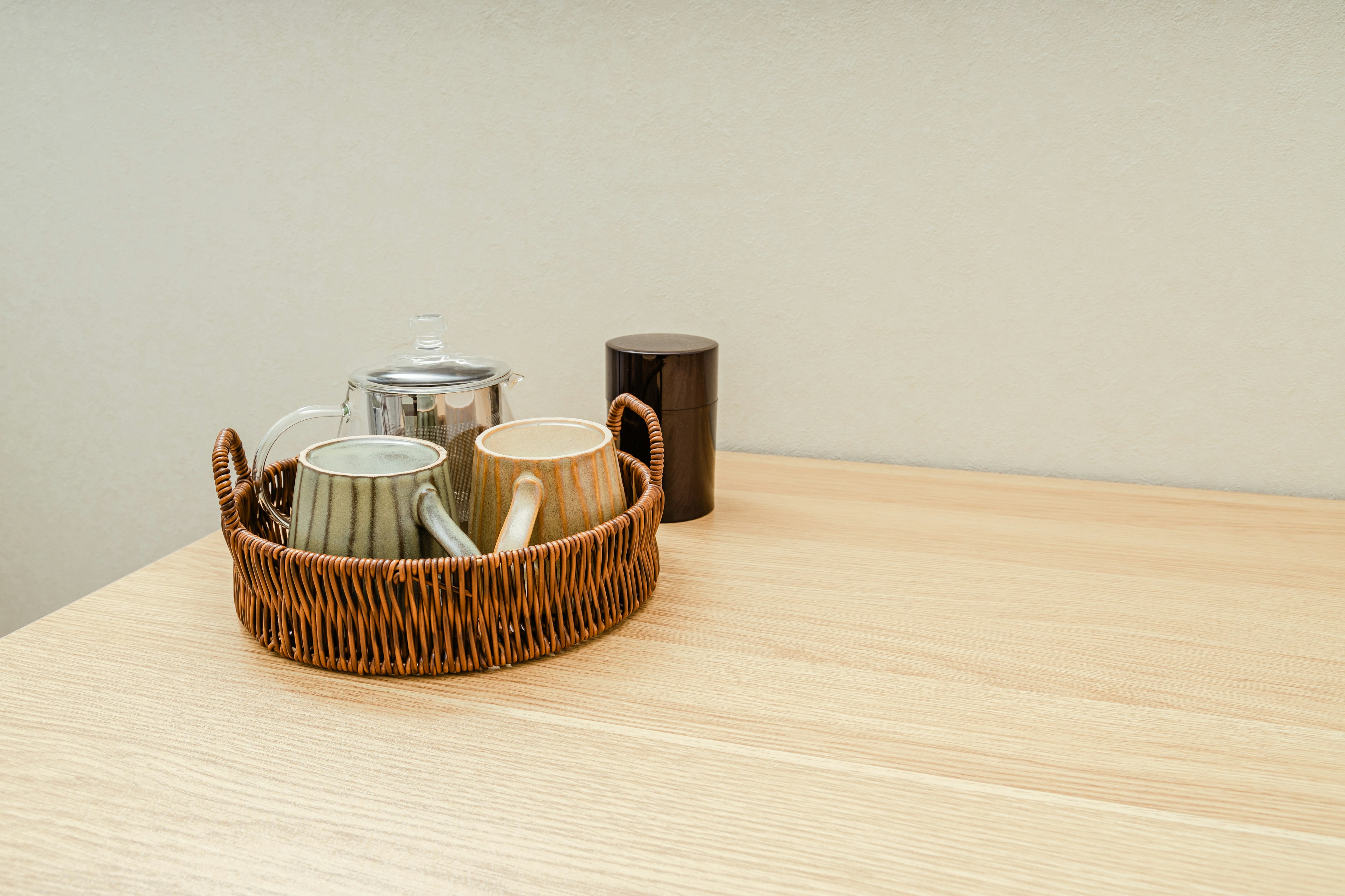 A basket containing cups and a teapot on a wooden table