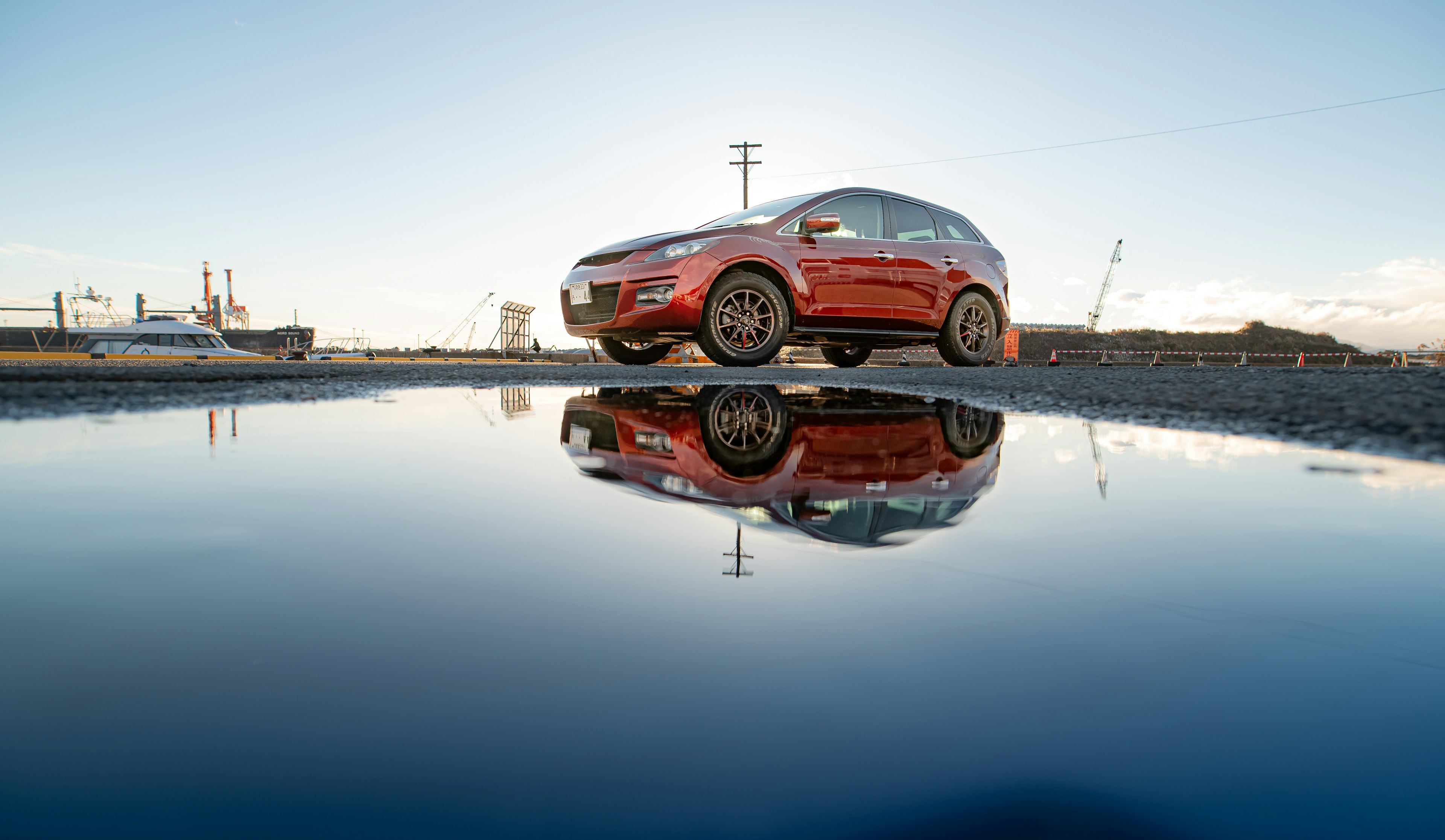 Red car reflected in a puddle under a clear blue sky