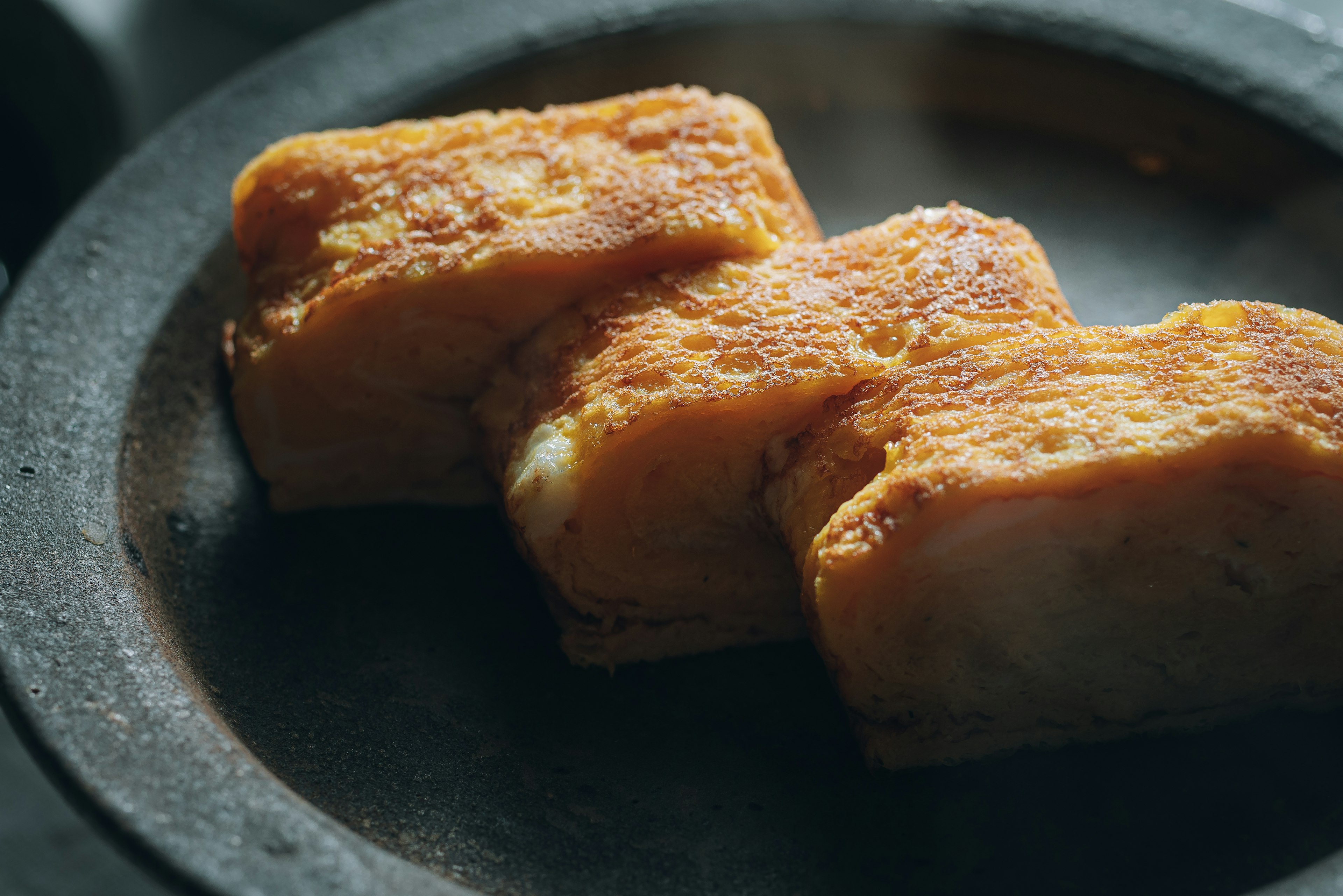 Three golden-brown tofu pieces on a dark plate