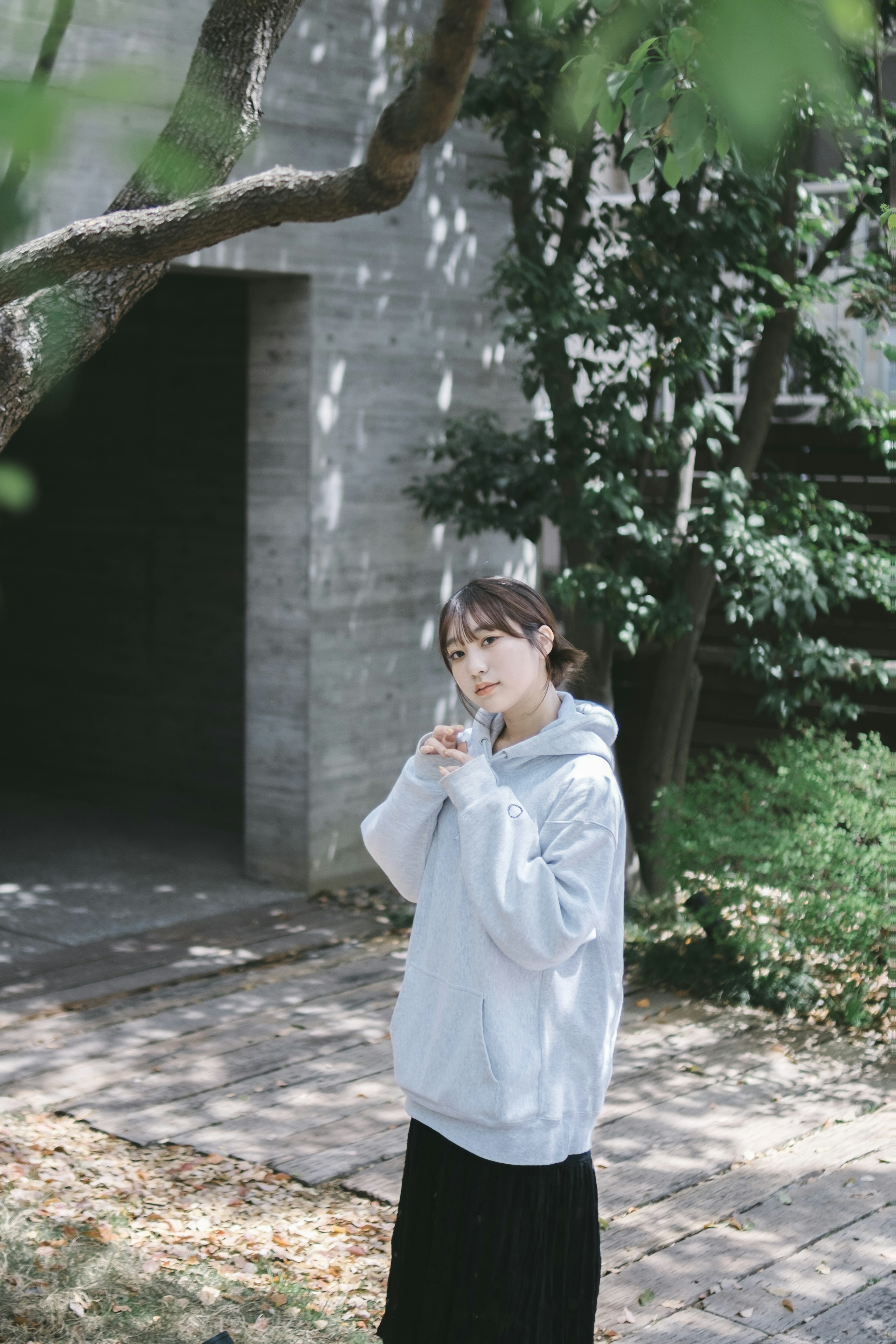 Una mujer posando bajo un árbol con una sudadera gris y una falda negra en un entorno natural sereno