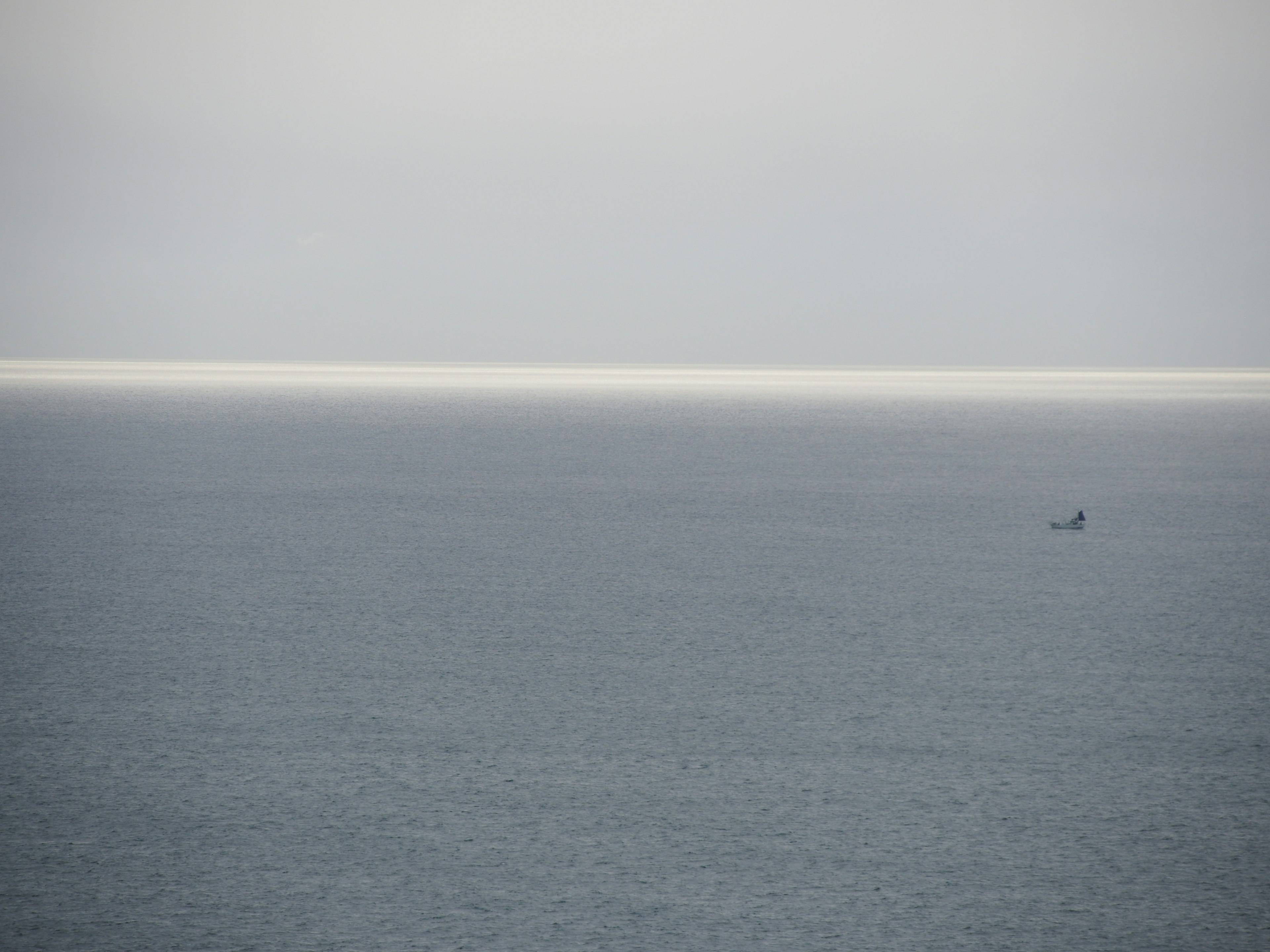 Overcast sky above a calm sea with a distant small boat