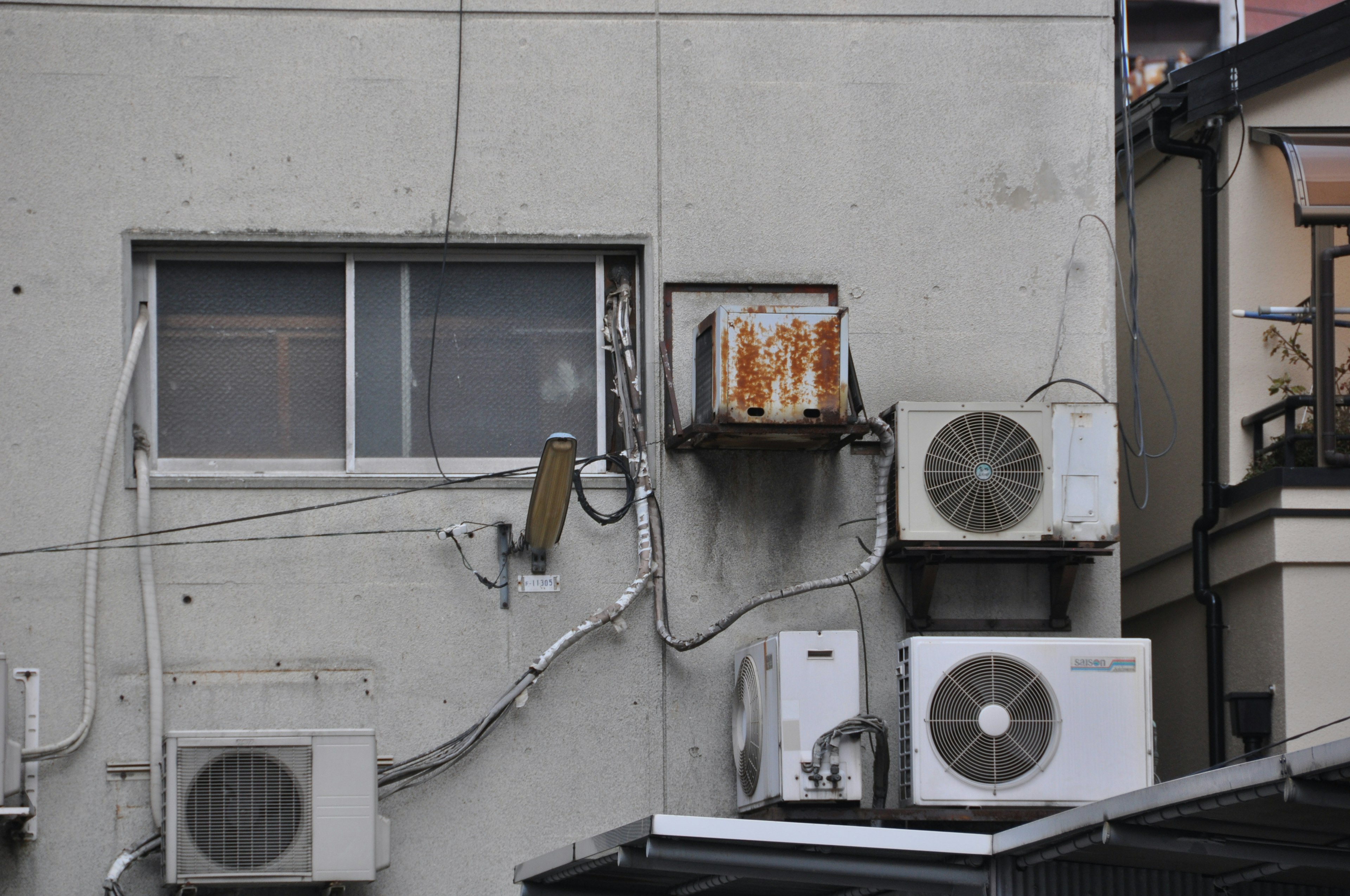 Air conditioning units mounted on an aging building wall with a window