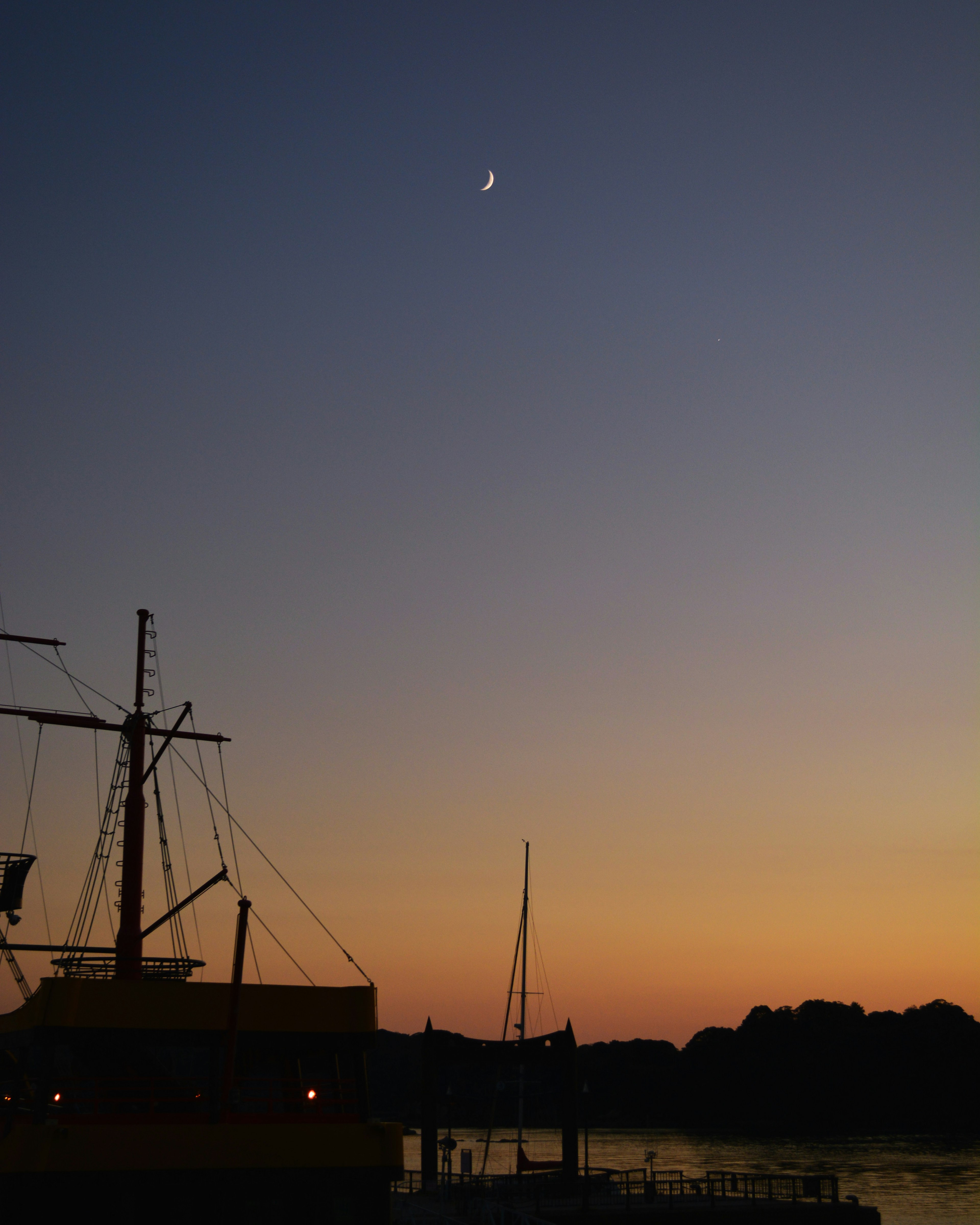 Une belle scène avec un bateau en silhouette contre un ciel de coucher de soleil et un croissant de lune