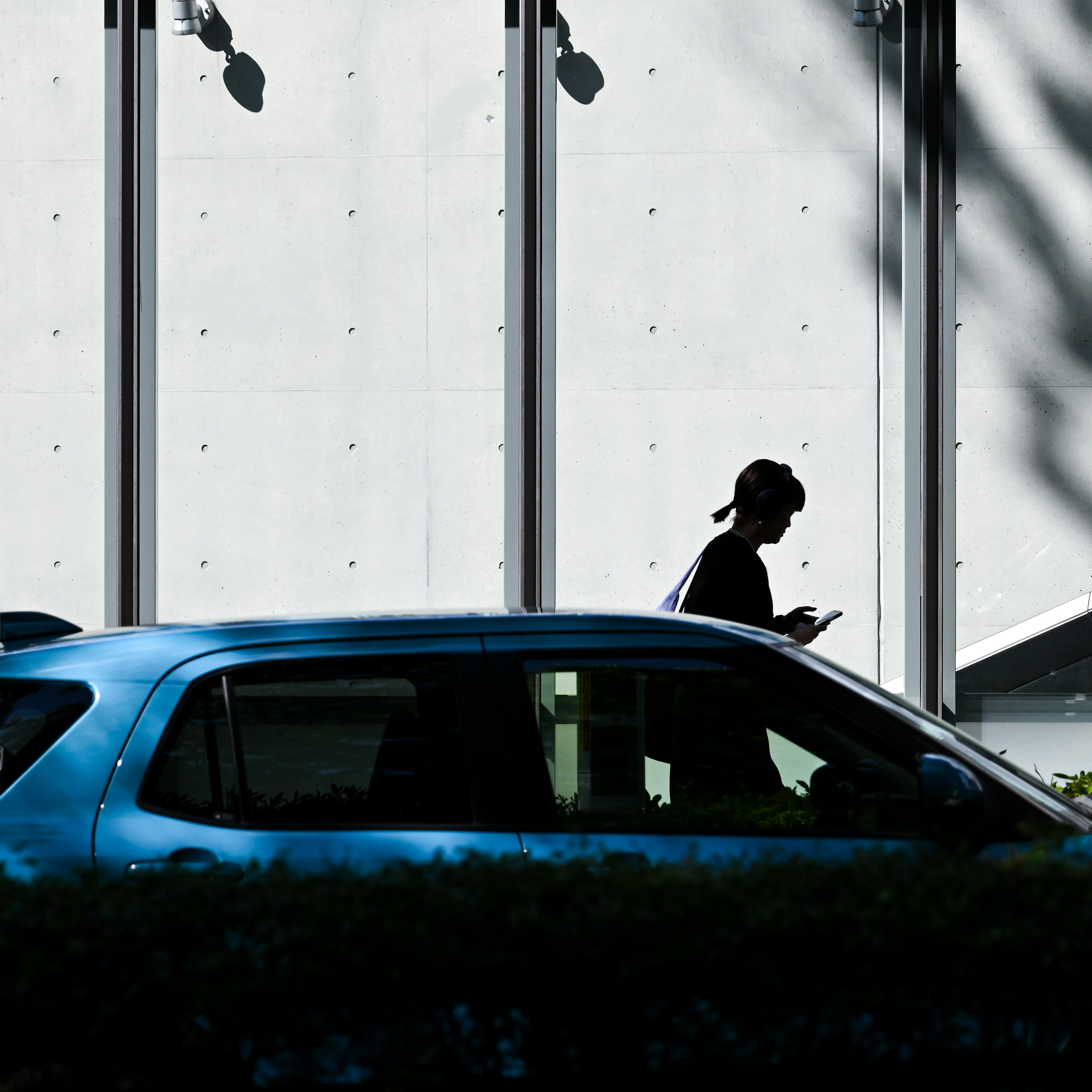 Silhouette de una persona caminando junto a un coche azul con una pared de edificio moderno