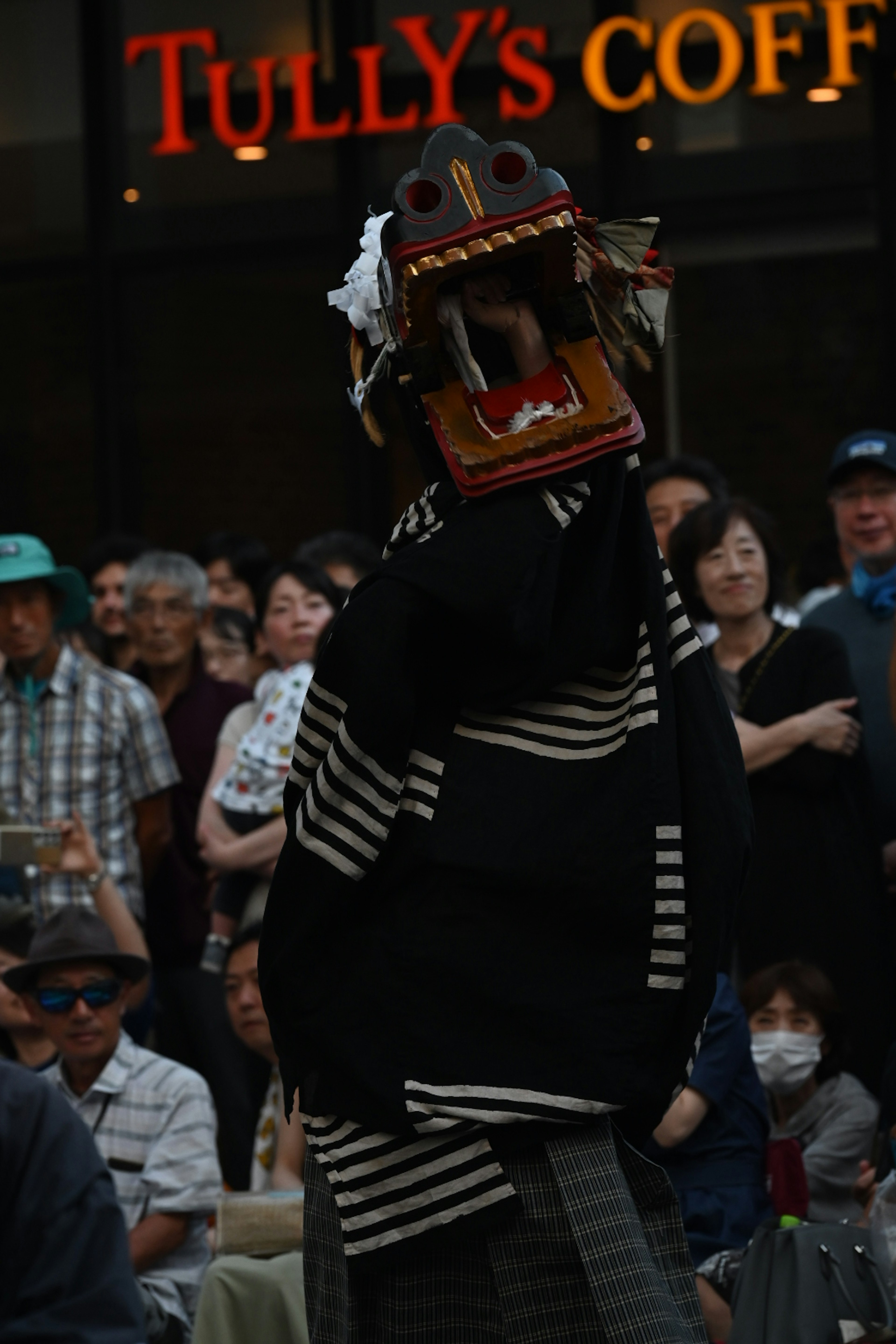 Person wearing traditional attire with a lion dance head in front of a Tully's Coffee sign