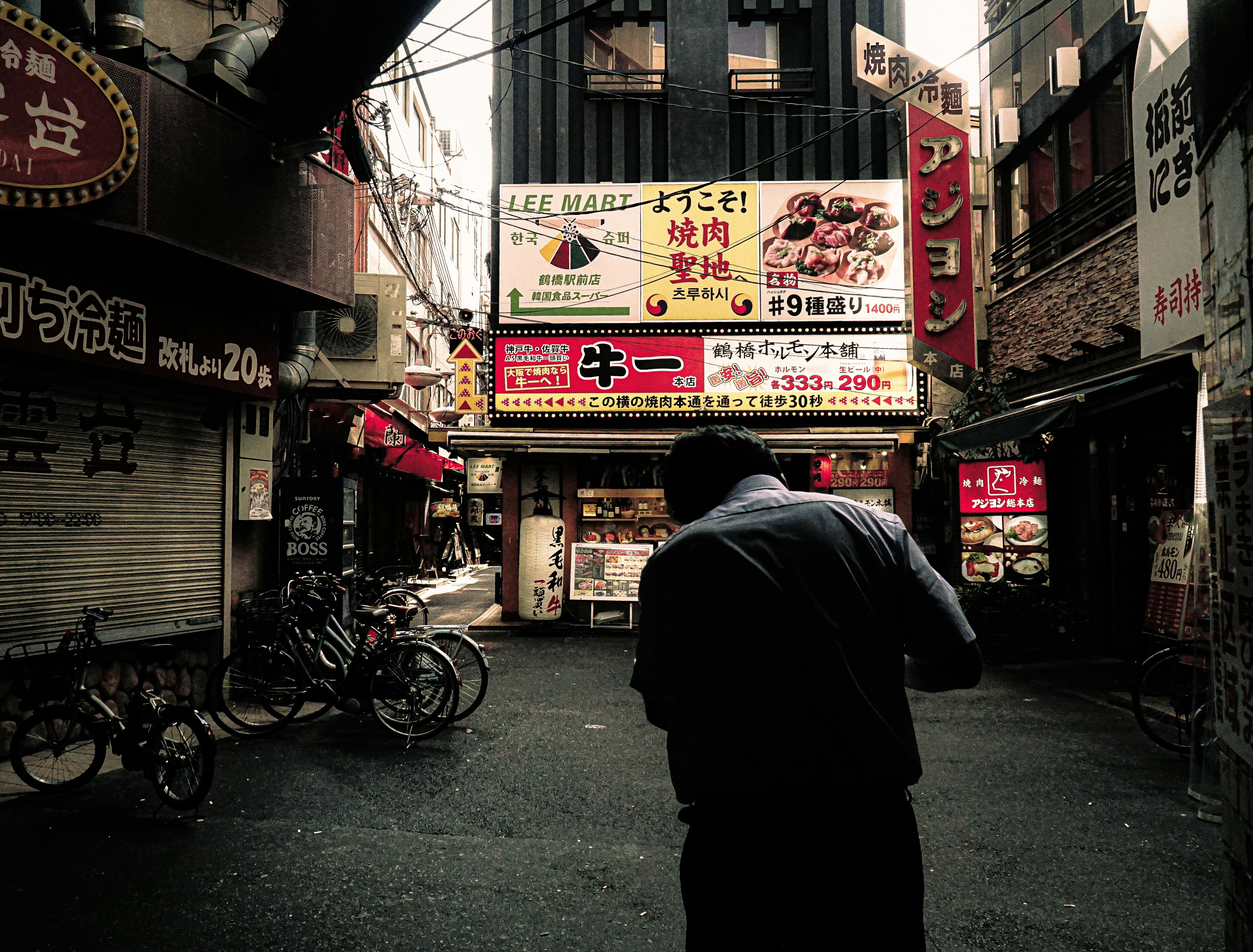 A man standing in a narrow alley with restaurant signs in the background