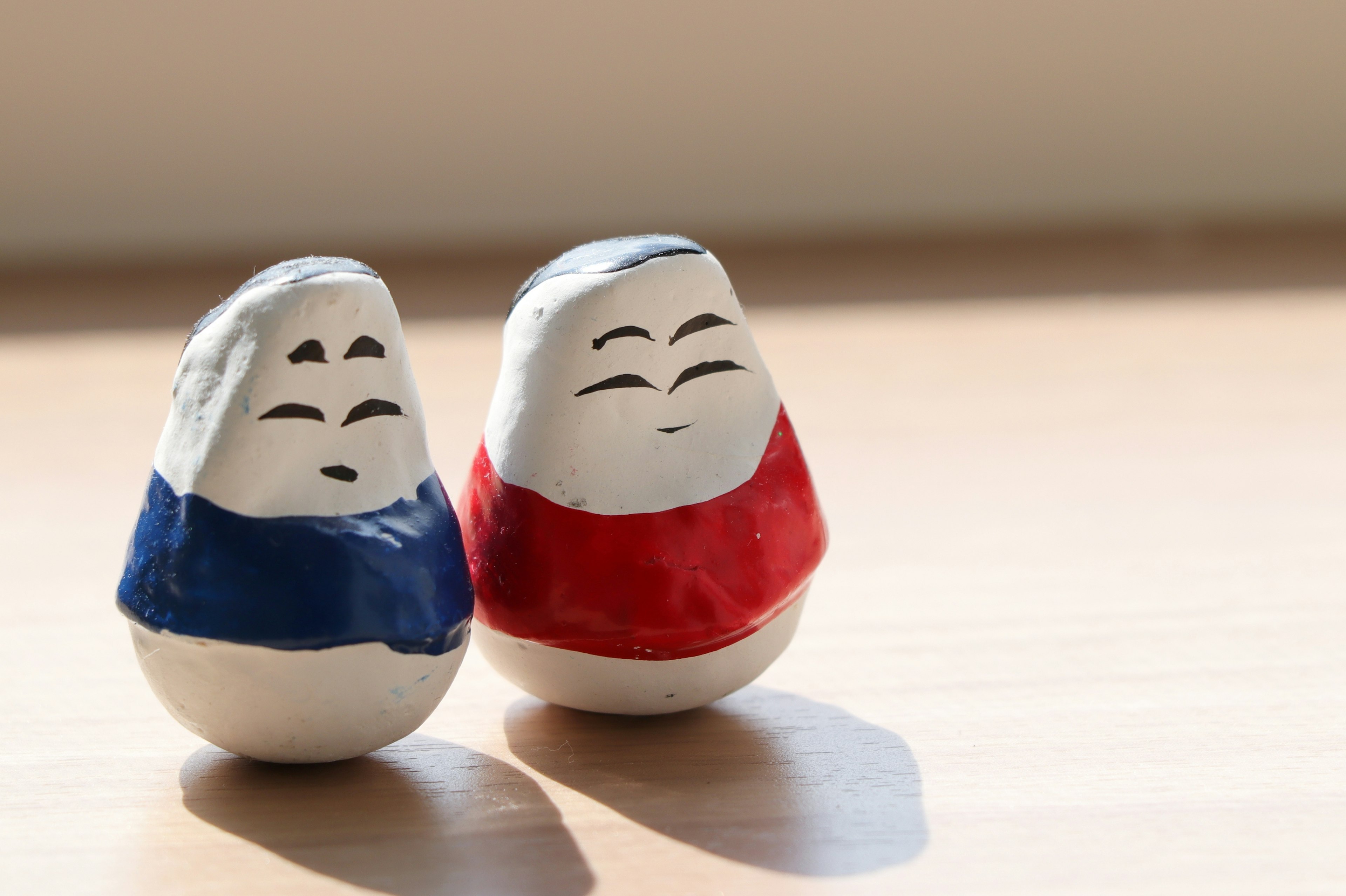 Two ceramic dolls dressed in blue and red clothing standing side by side