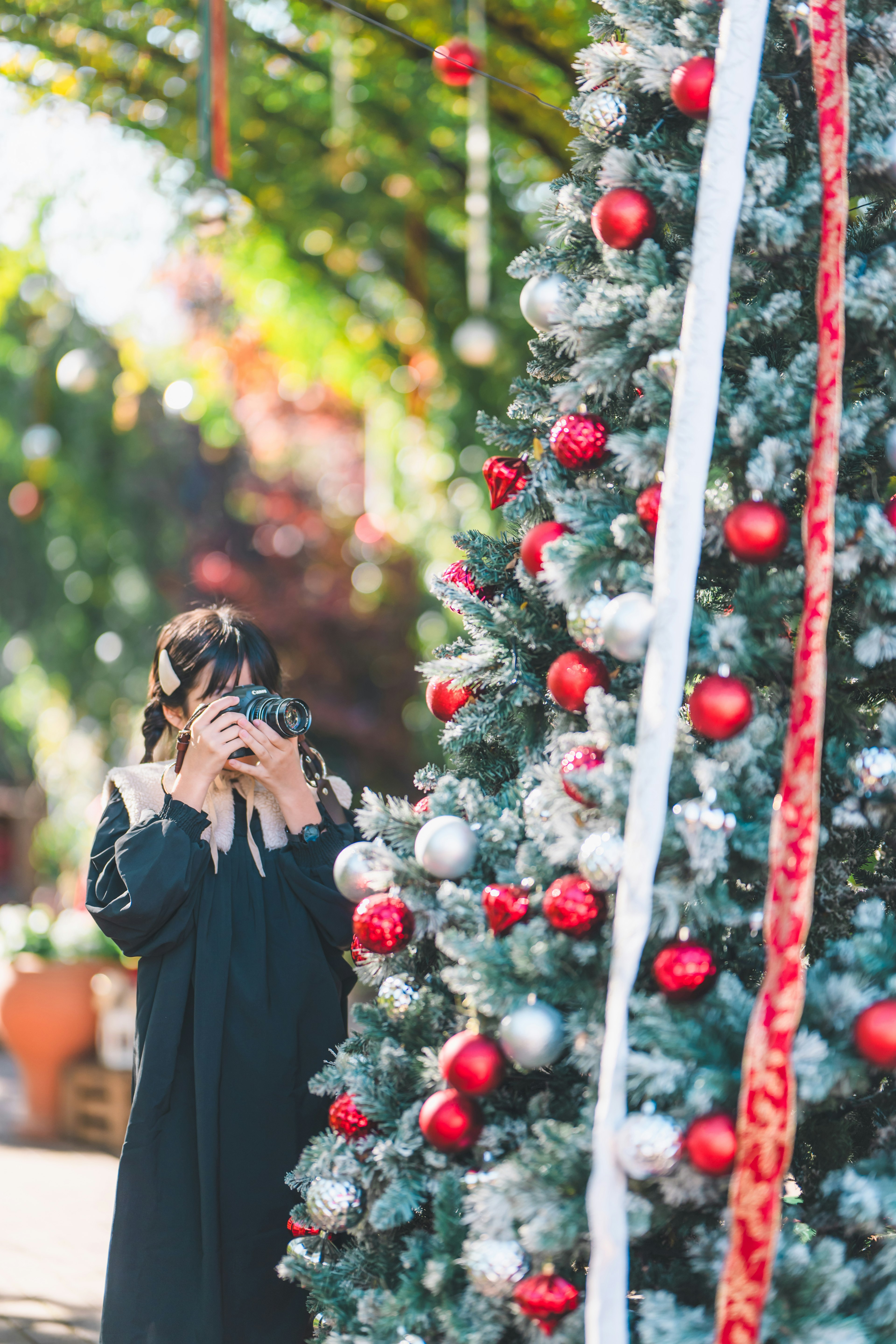 クリスマスツリーの前でカメラを持つ女性の写真赤と銀のオーナメントが飾られたツリー