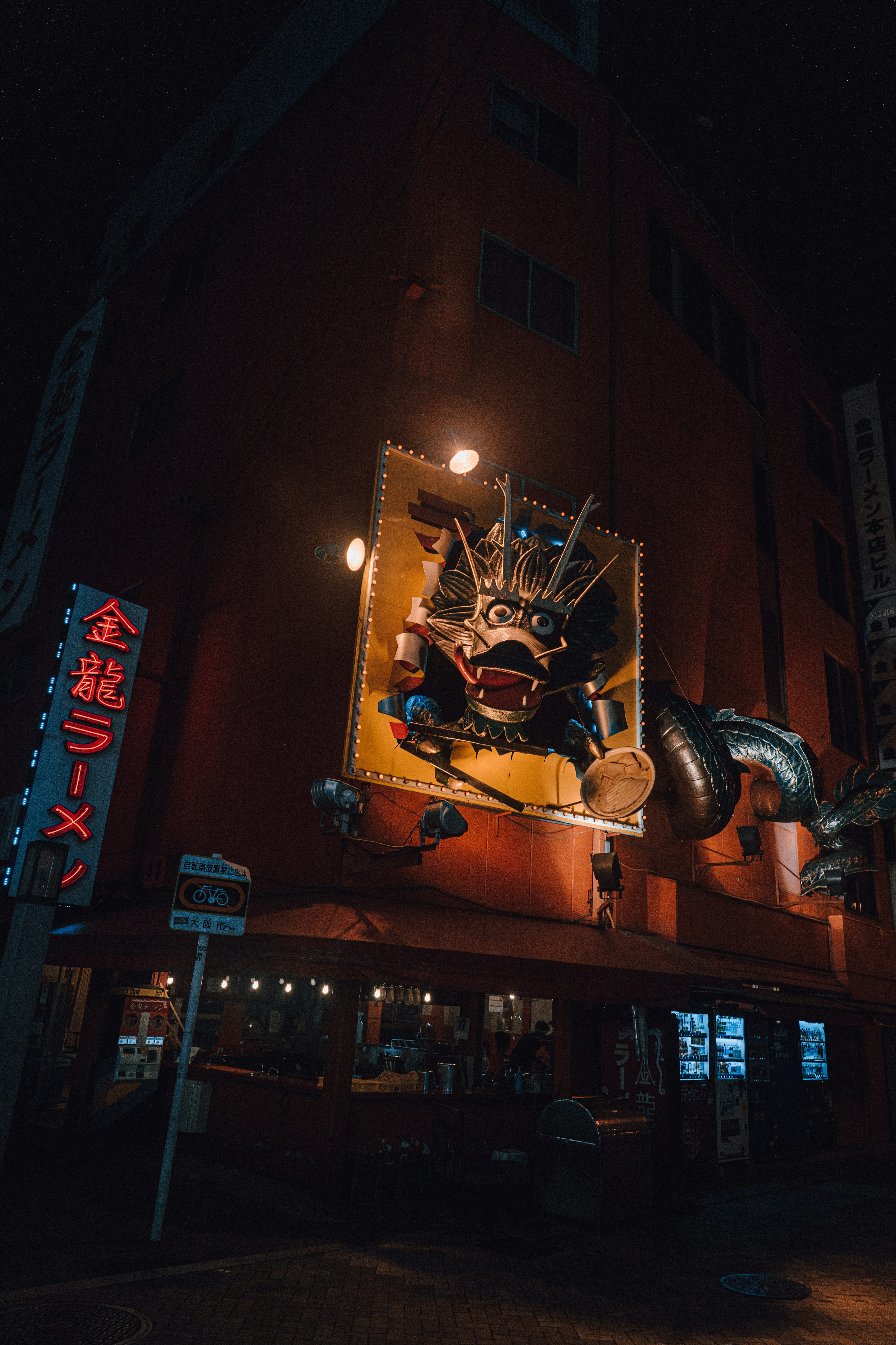 Nachtansicht eines Ramen-Restaurants mit Drachenskulptur und Neonbeschilderung