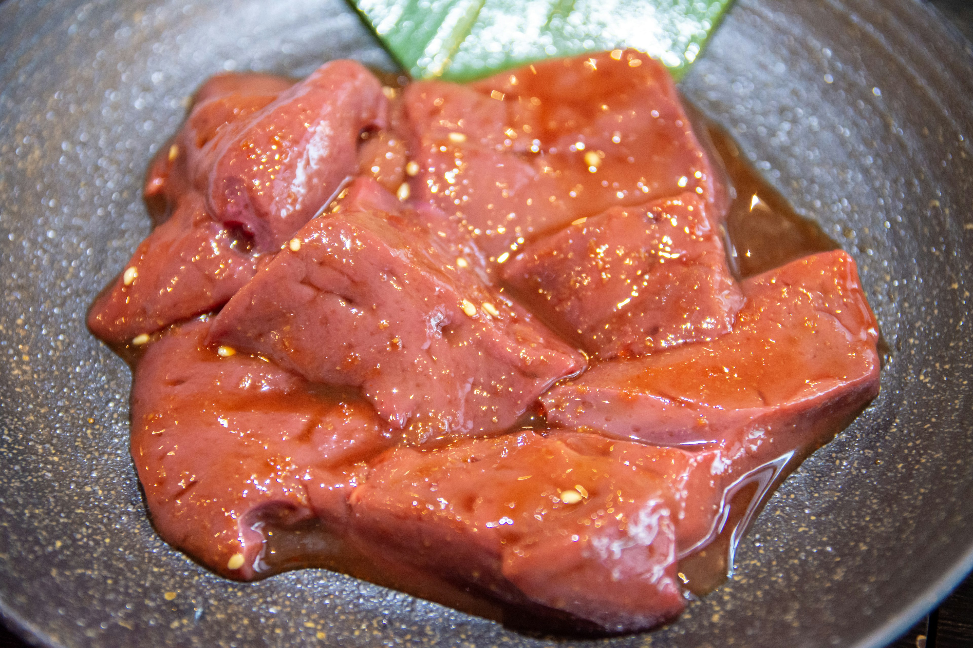 Chunks of red meat marinated on a black plate with a green leaf