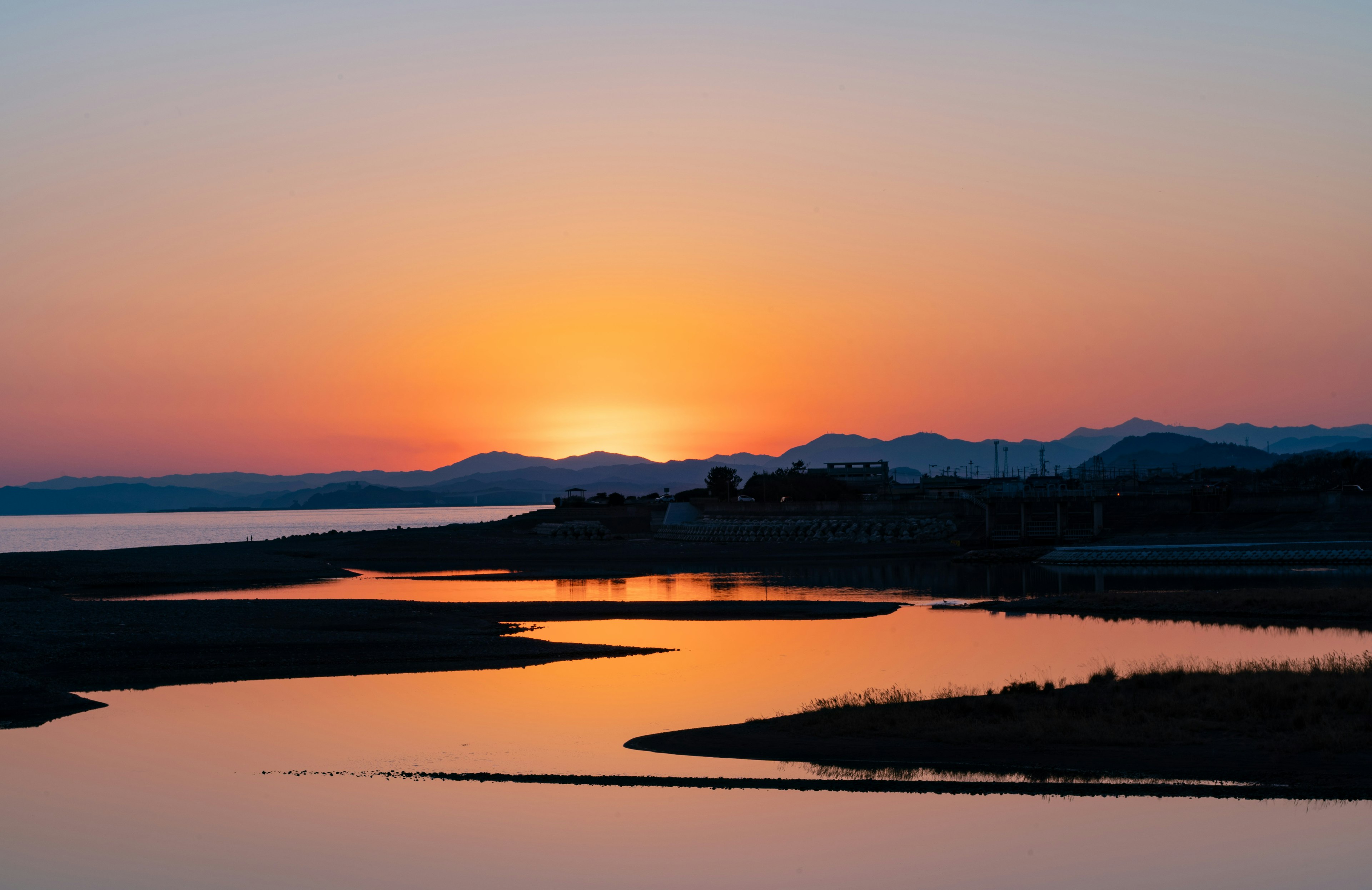 夕日が沈む海岸の風景 水面に映るオレンジ色の空と山影