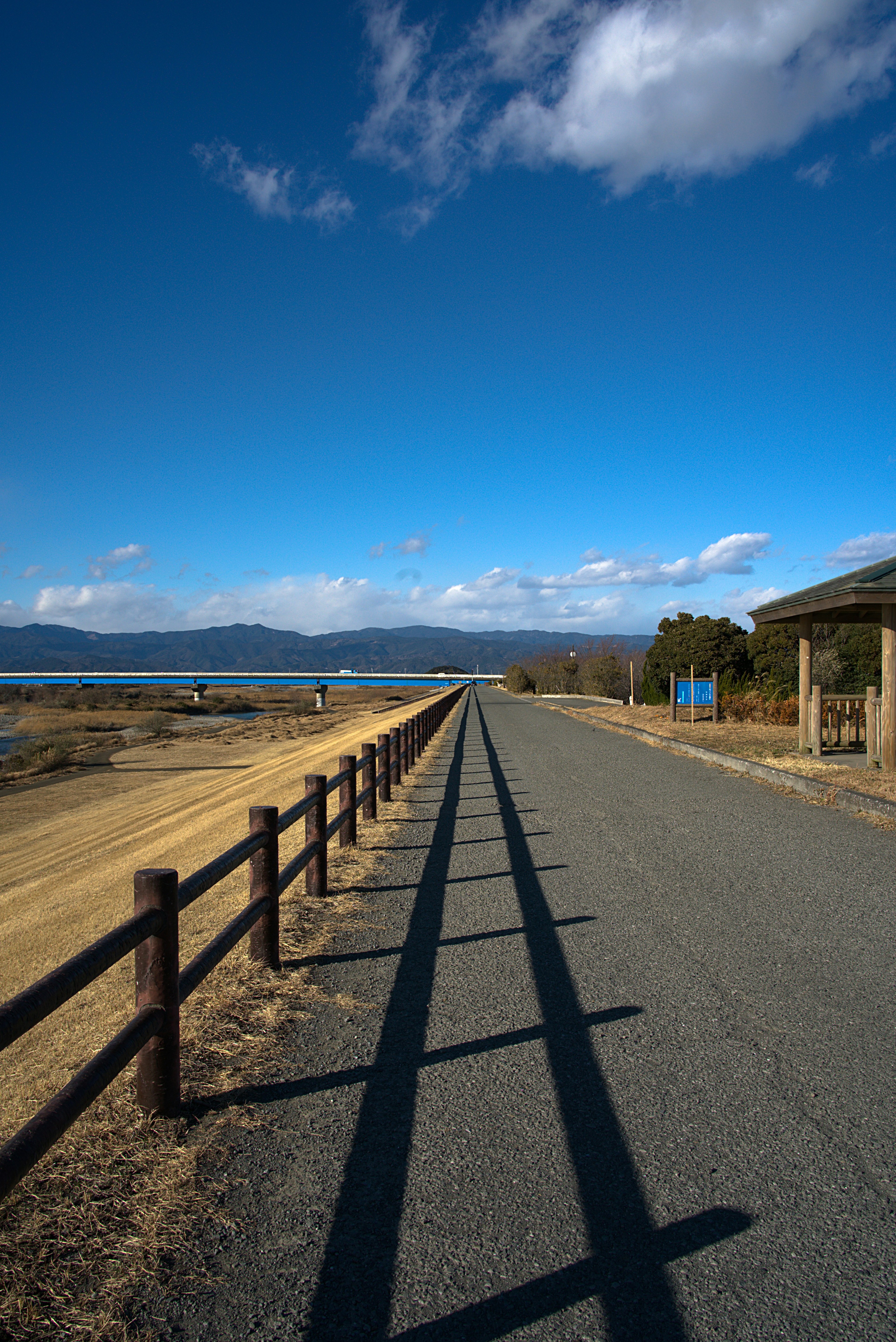 Paved road with wooden fence under a blue sky and scattered clouds