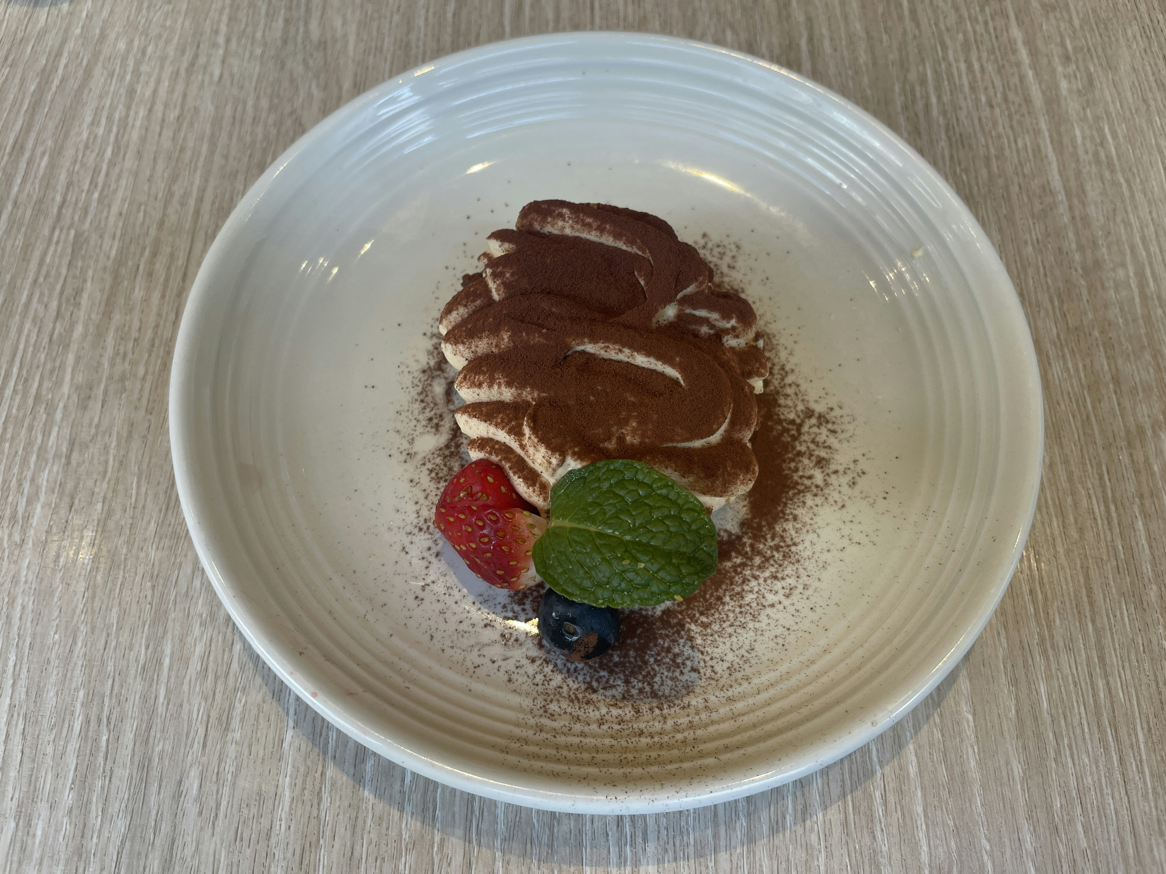 Postre de tiramisú decorado con crema y cacao acompañado de bayas y menta