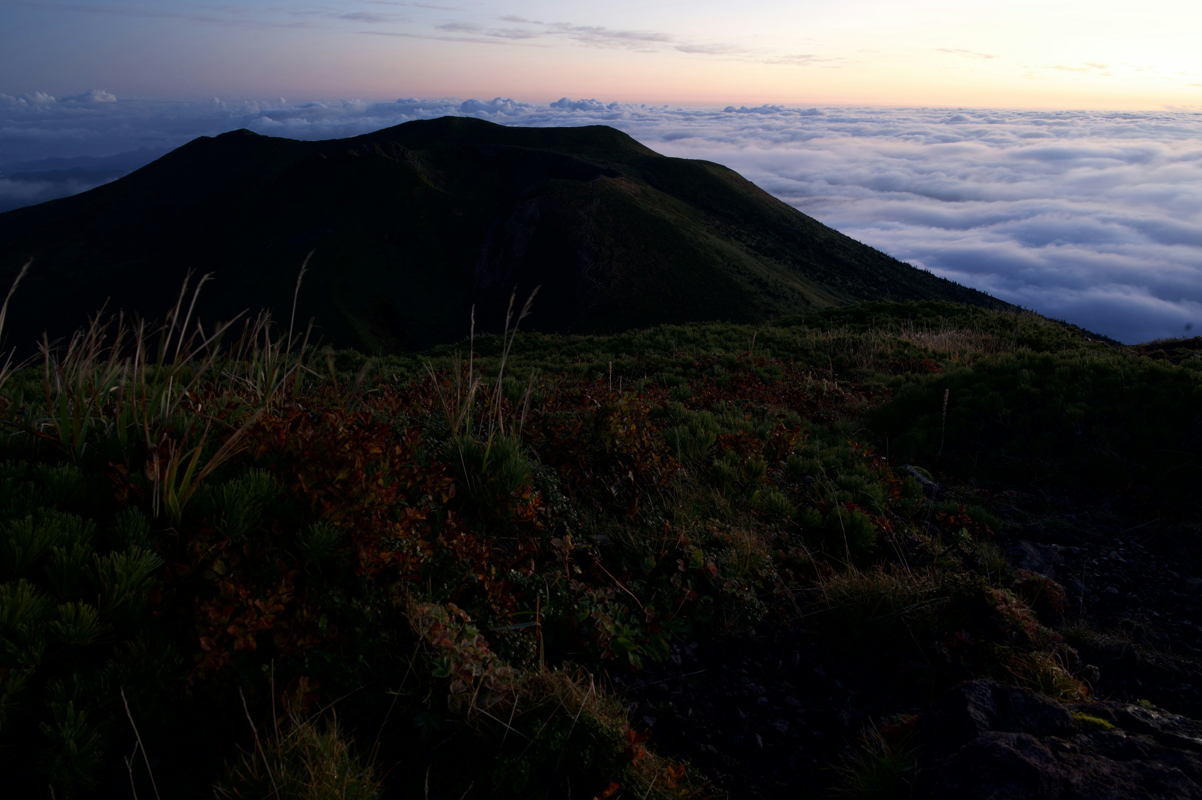 Siluet gunung di atas lautan awan saat matahari terbenam