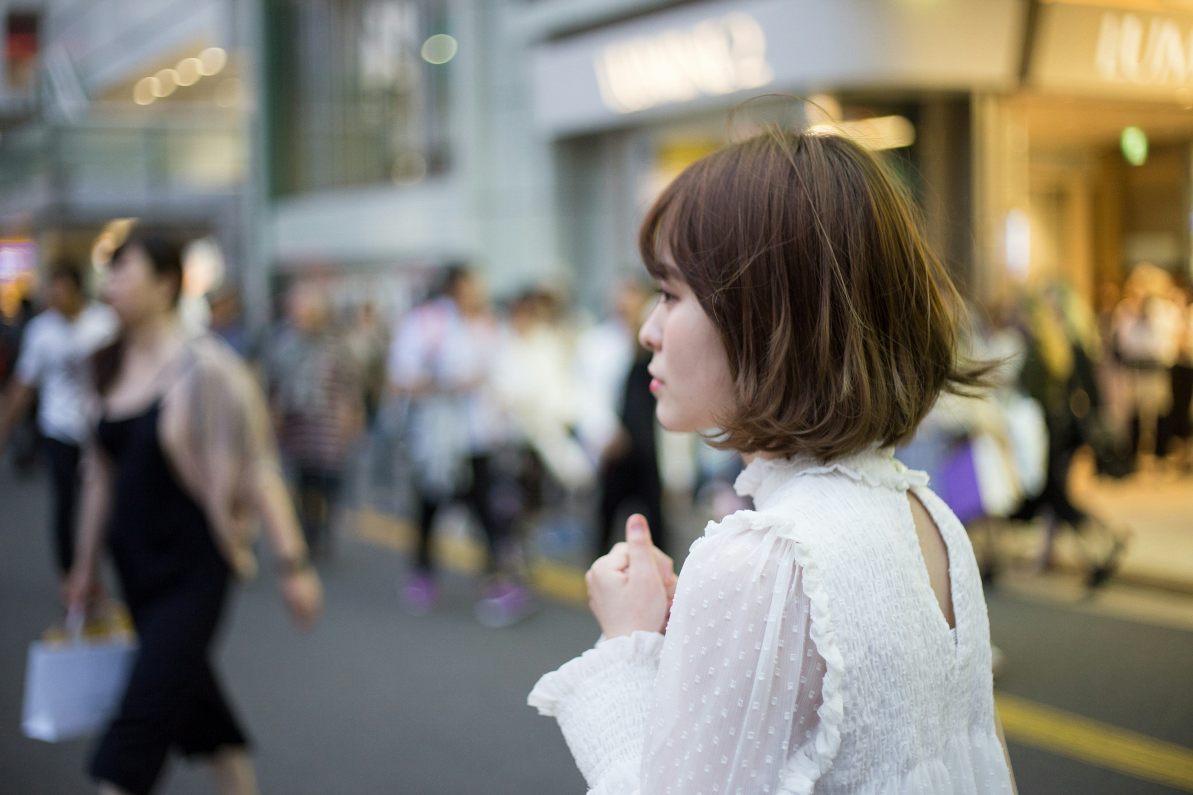 A woman in a white blouse walking on the street with blurred pedestrians in the background