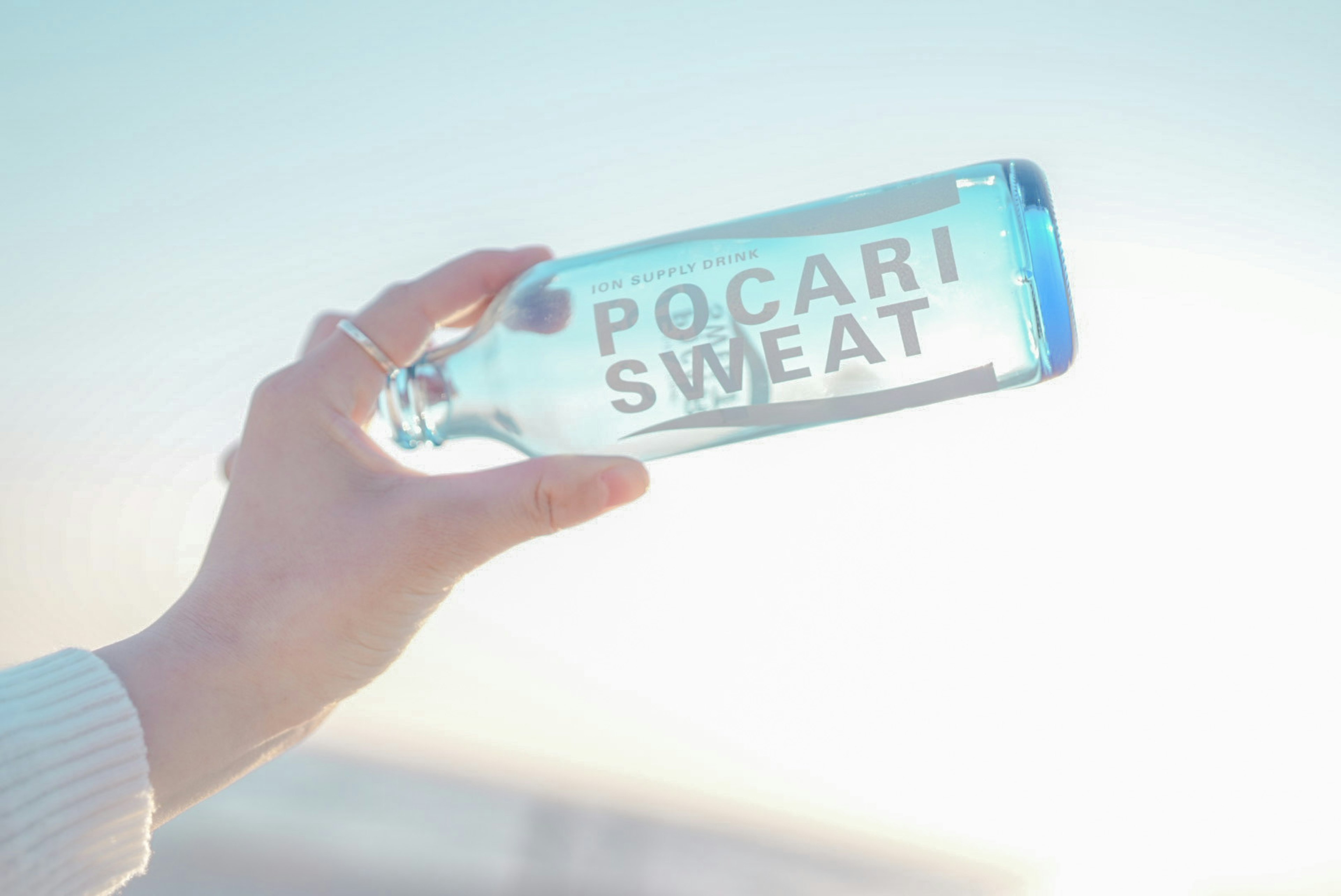 Tangan memegang botol Pocari Sweat biru di latar belakang terang