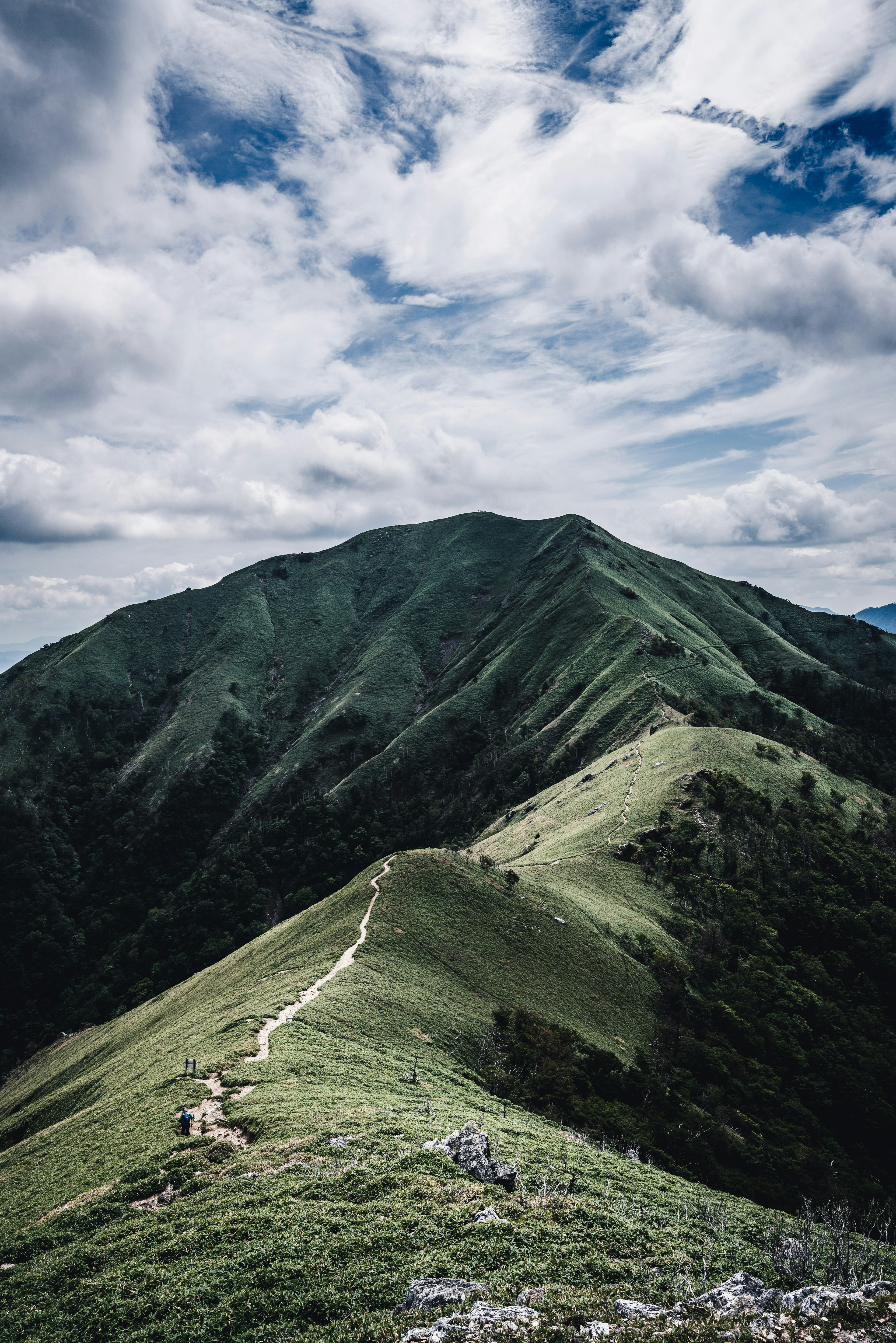 綠色山丘的風景和曲折小路在多雲的天空下