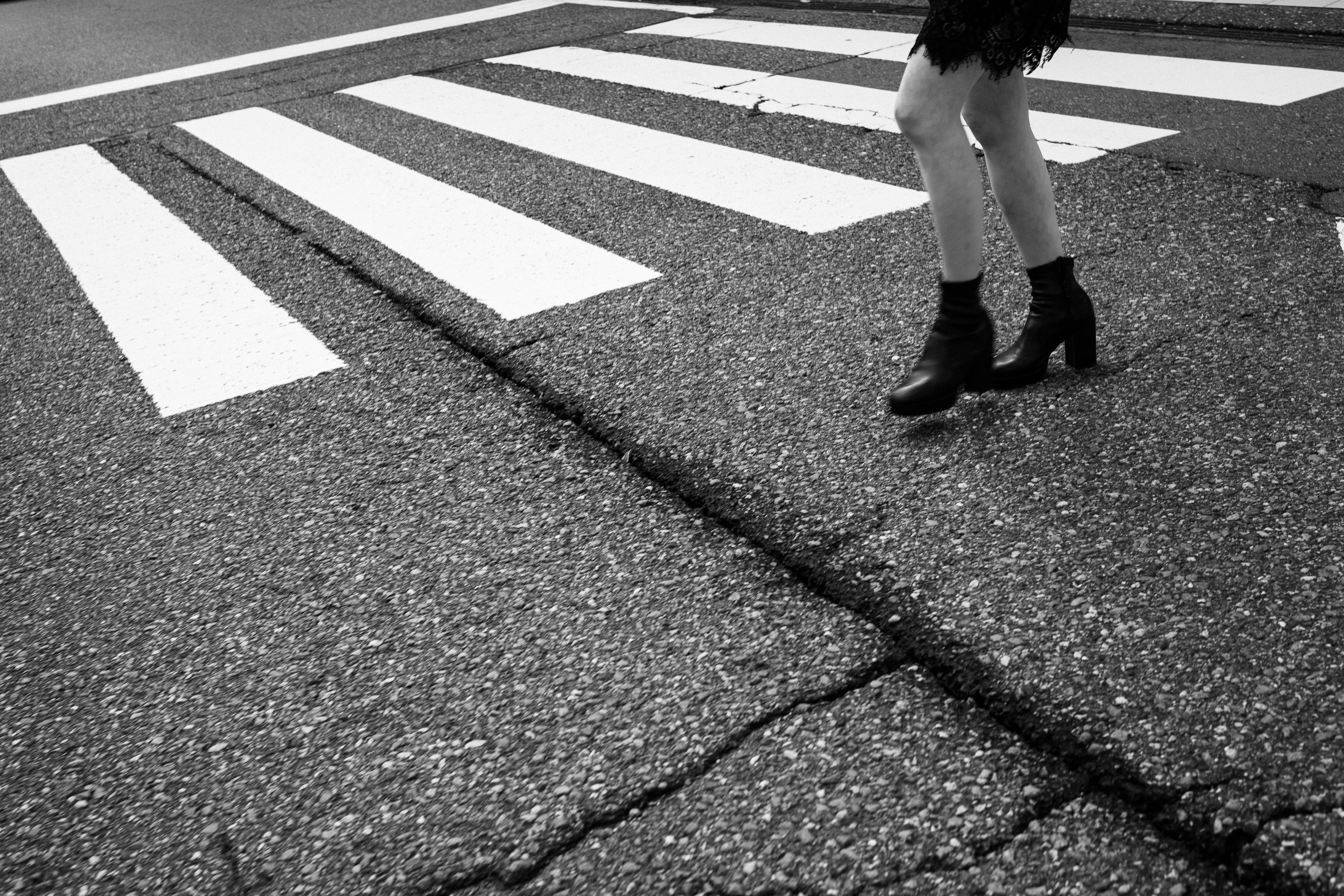 Las piernas y las botas de una mujer caminando sobre un paso de cebra en blanco y negro