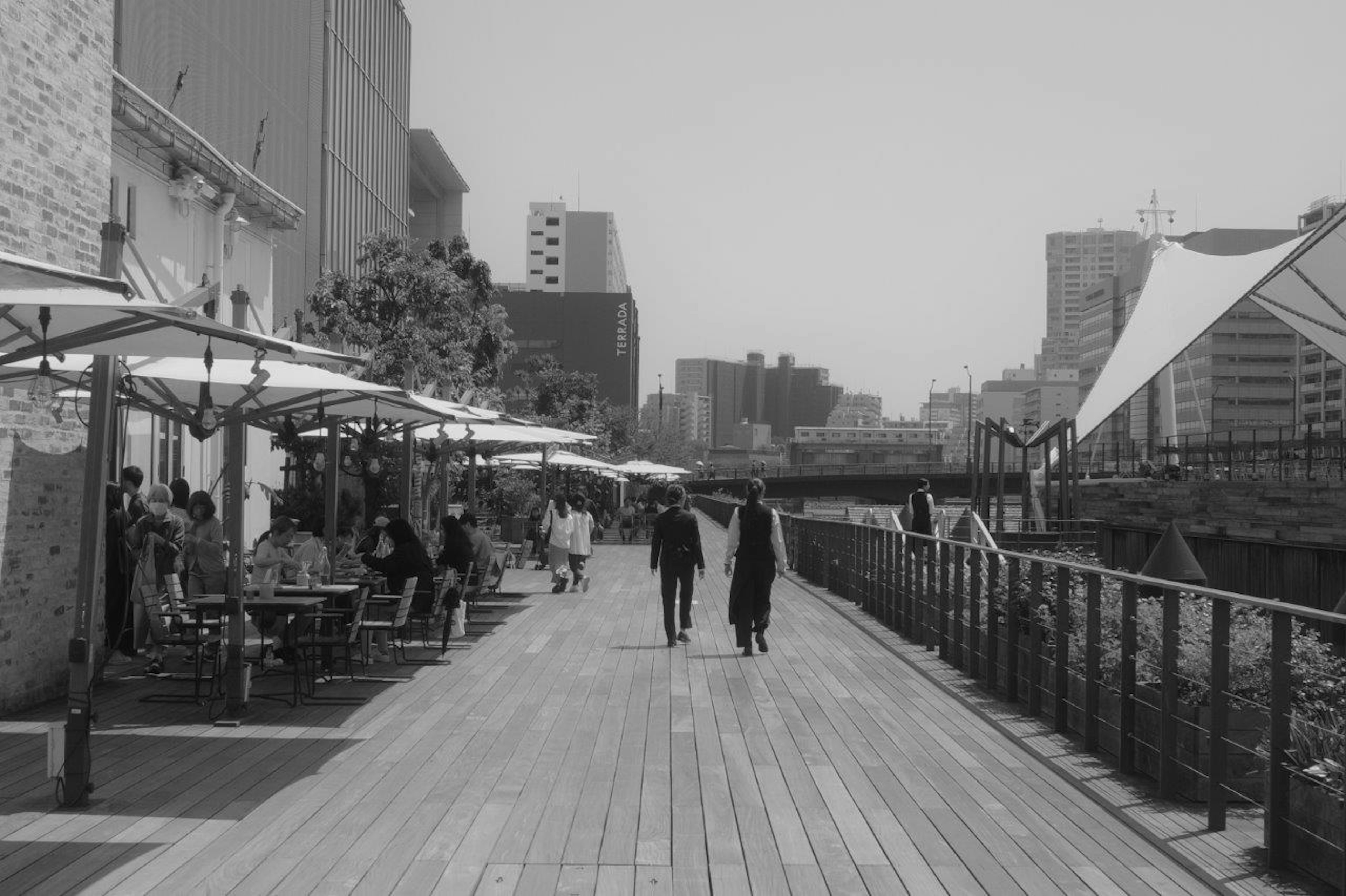 モノクロの川沿いの歩道にいるカップルとカフェのテラス