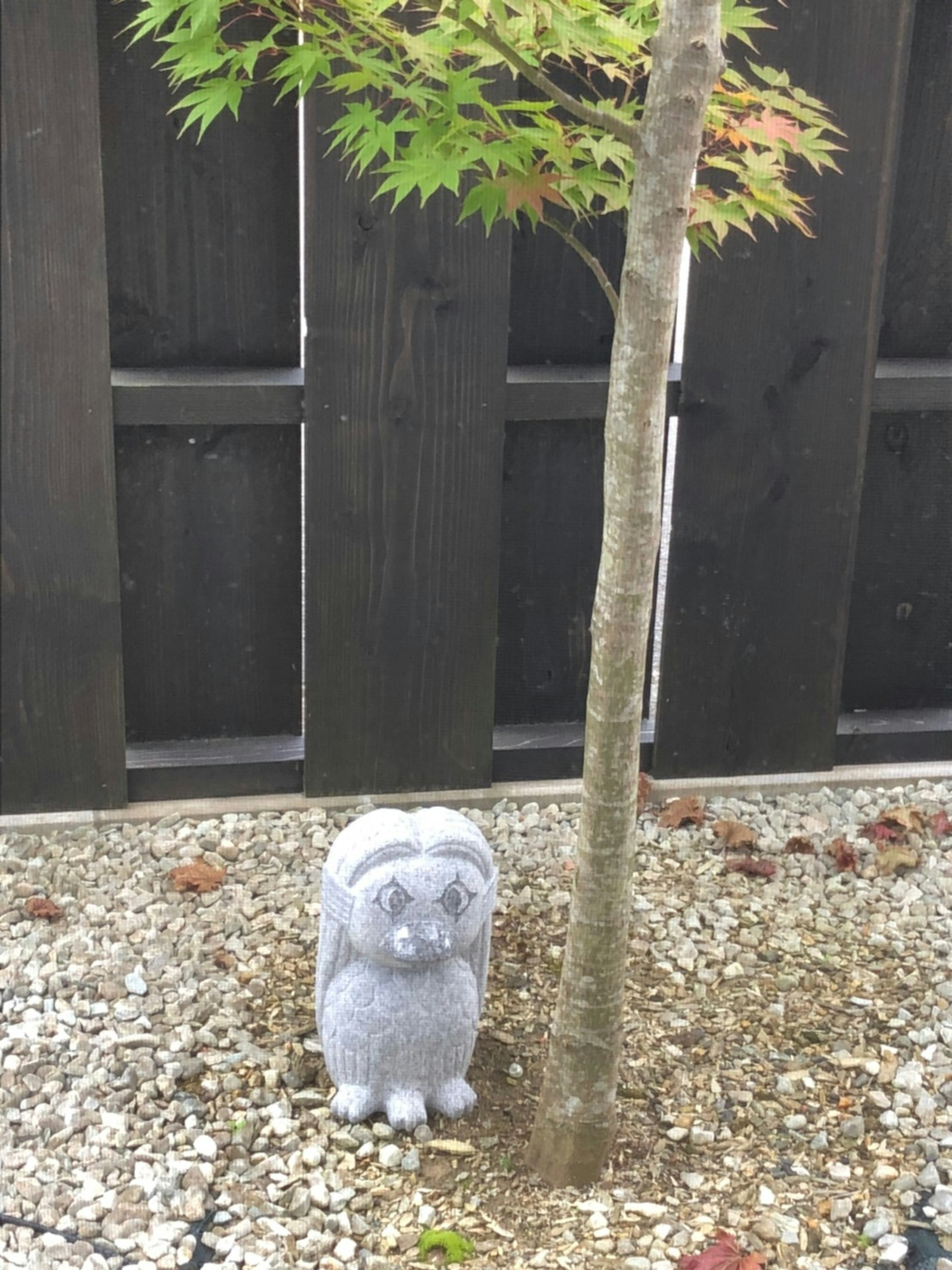 A small stone dog statue beside a tree in a garden