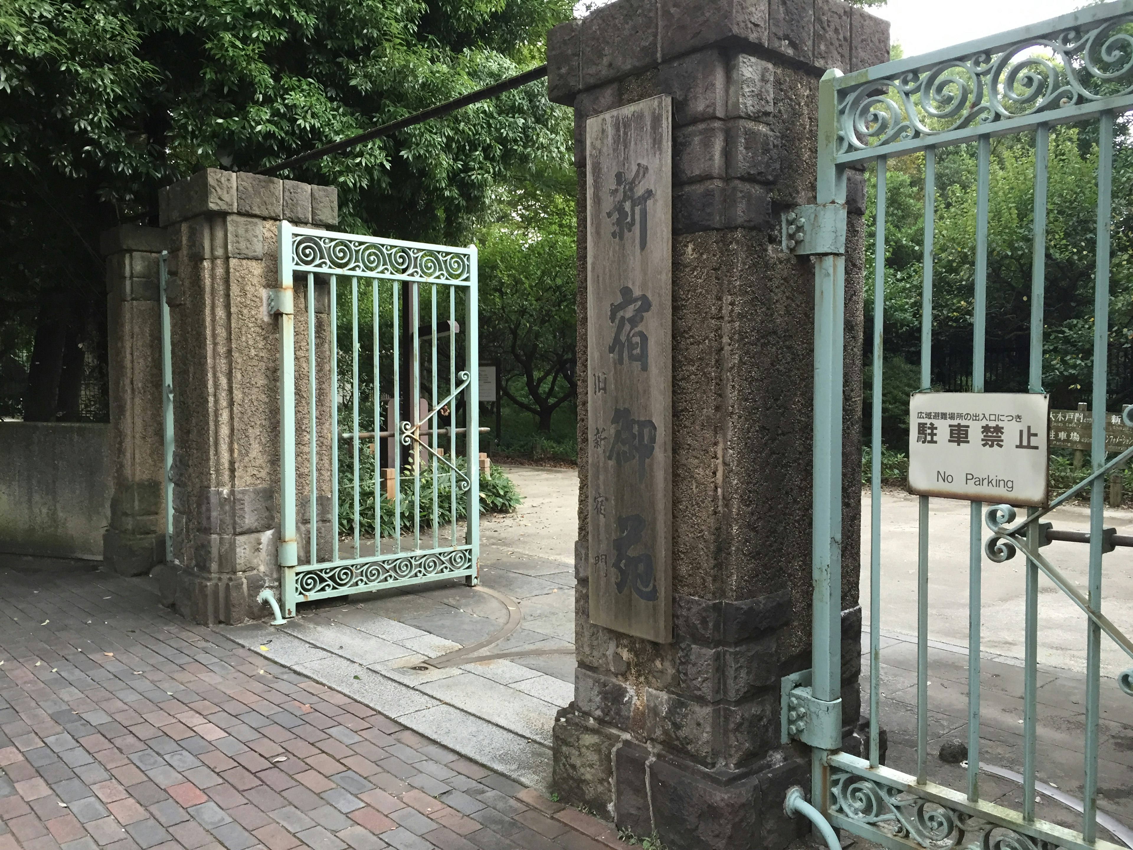 Entrada a un parque con puertas de hierro azules y pilares de piedra