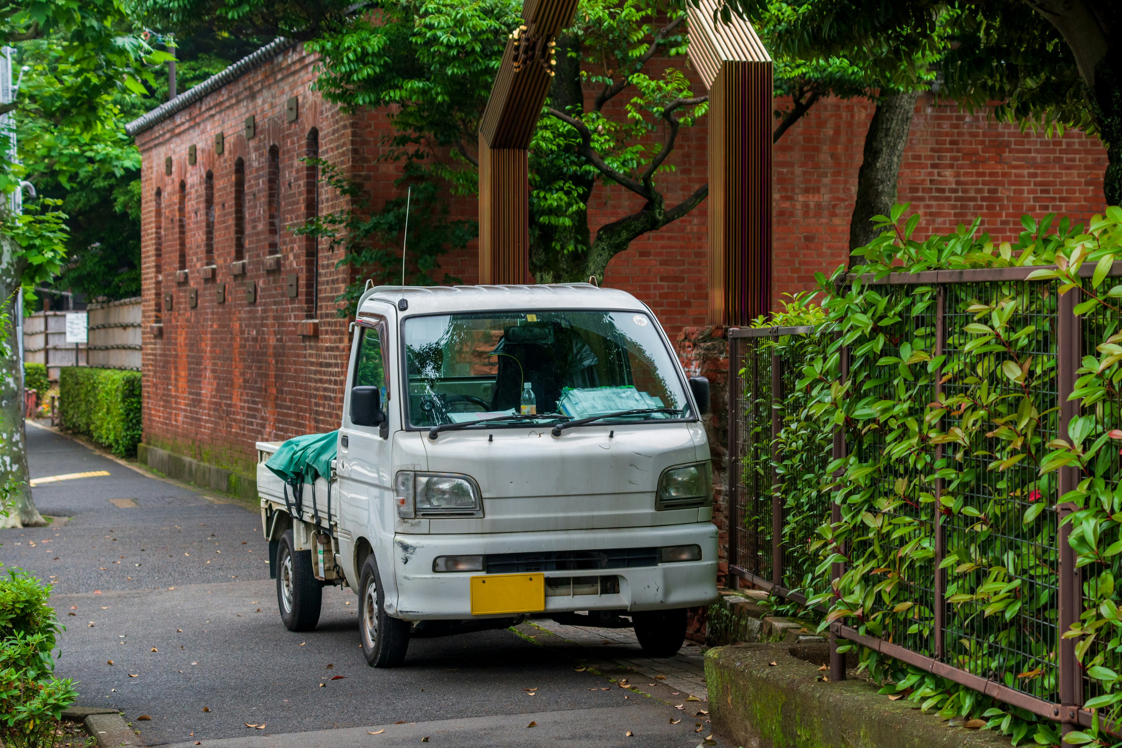 一輛白色小貨車停在綠色籬笆旁邊