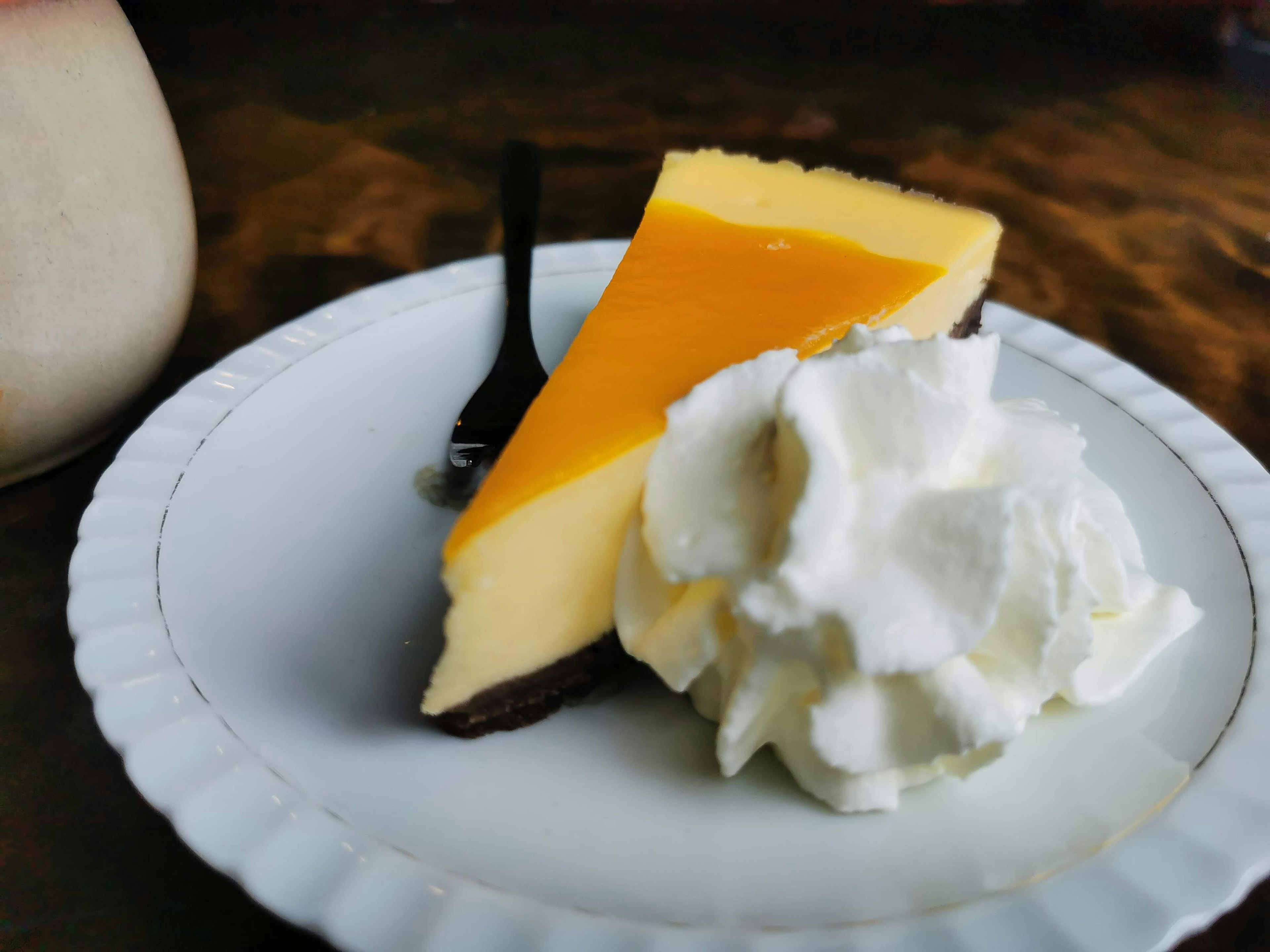 Una porción de cheesecake cubierta con glaseado amarillo y crema batida en un plato blanco