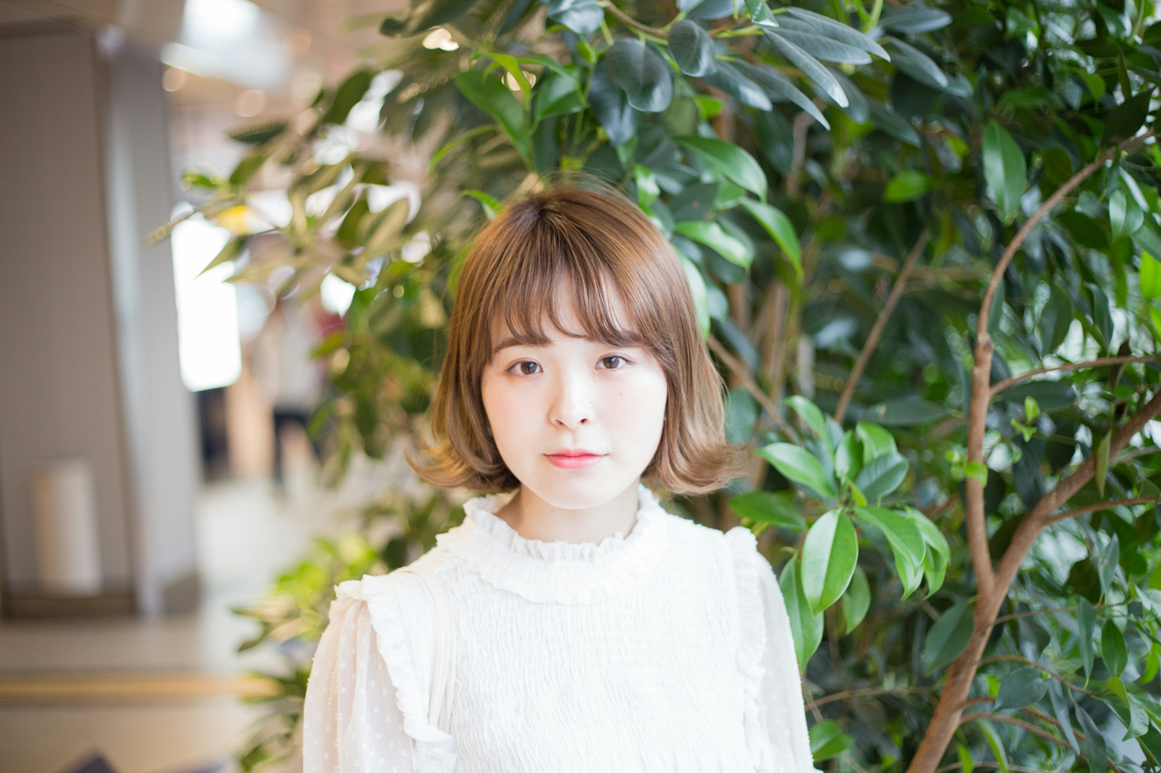 A woman in a white blouse standing in front of green plants