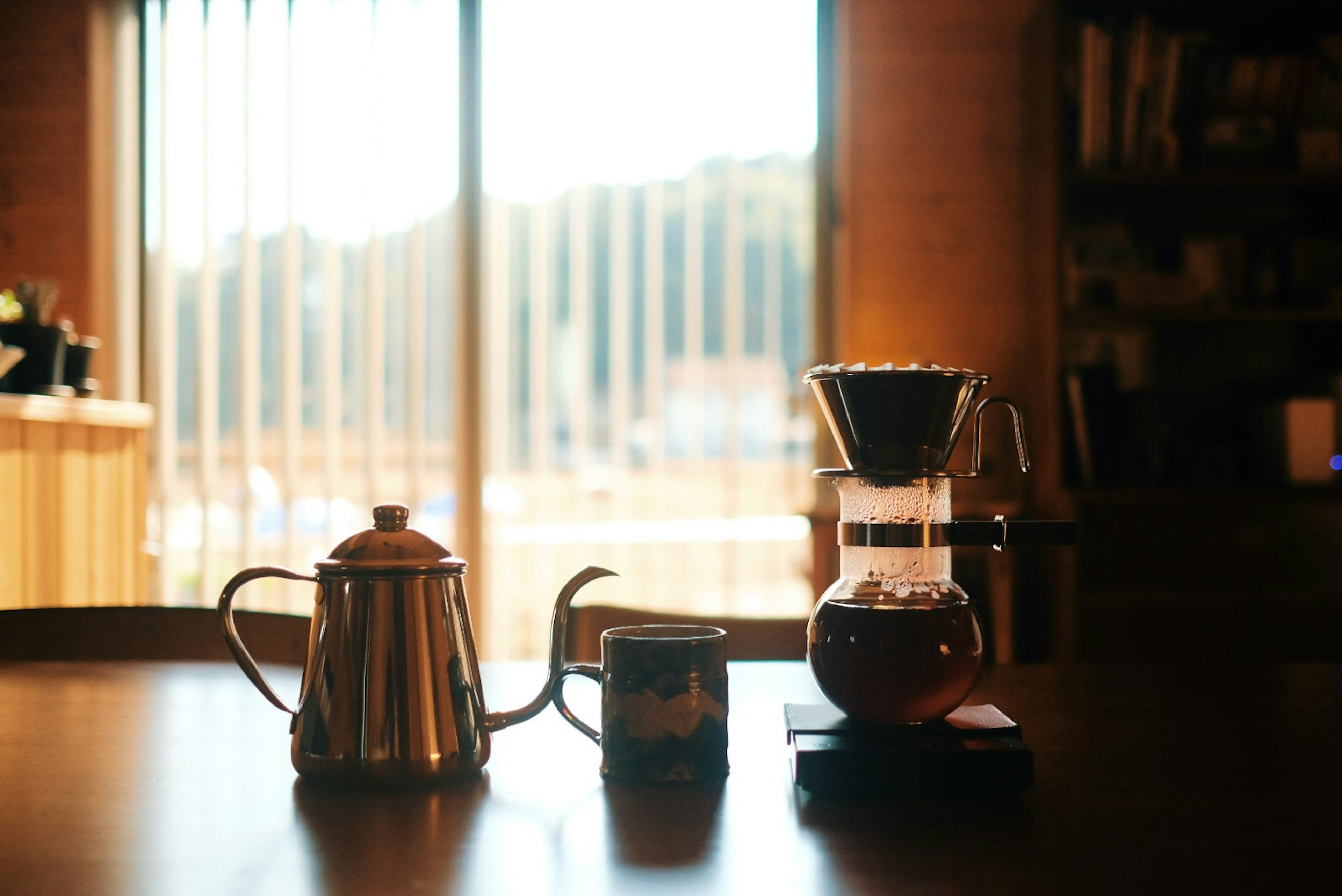 Sebuah mesin kopi dan teko di atas meja dengan cahaya alami masuk melalui jendela