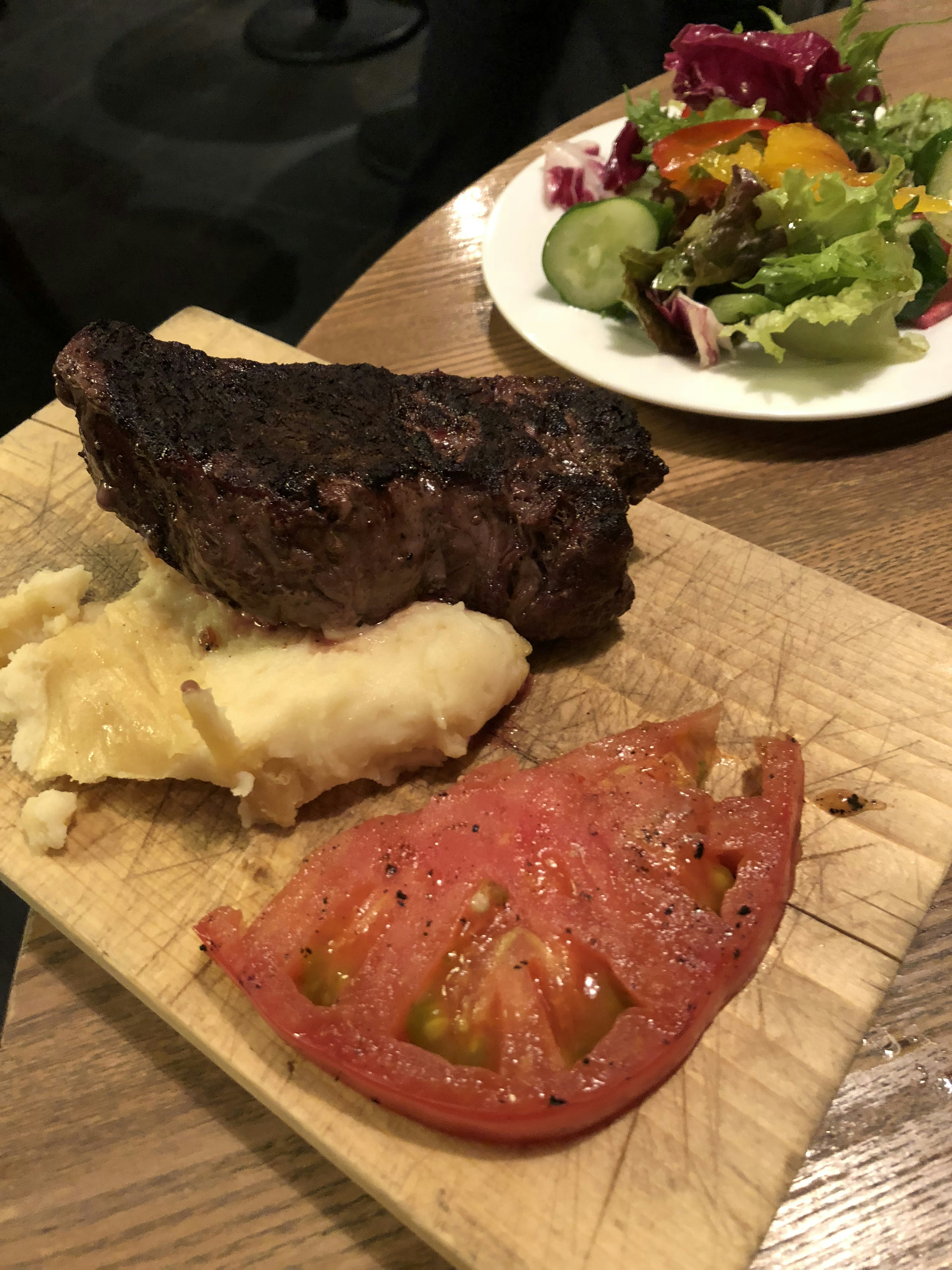 焼き肉とマッシュポテト、トマトのスライスが木のプレートに盛られている