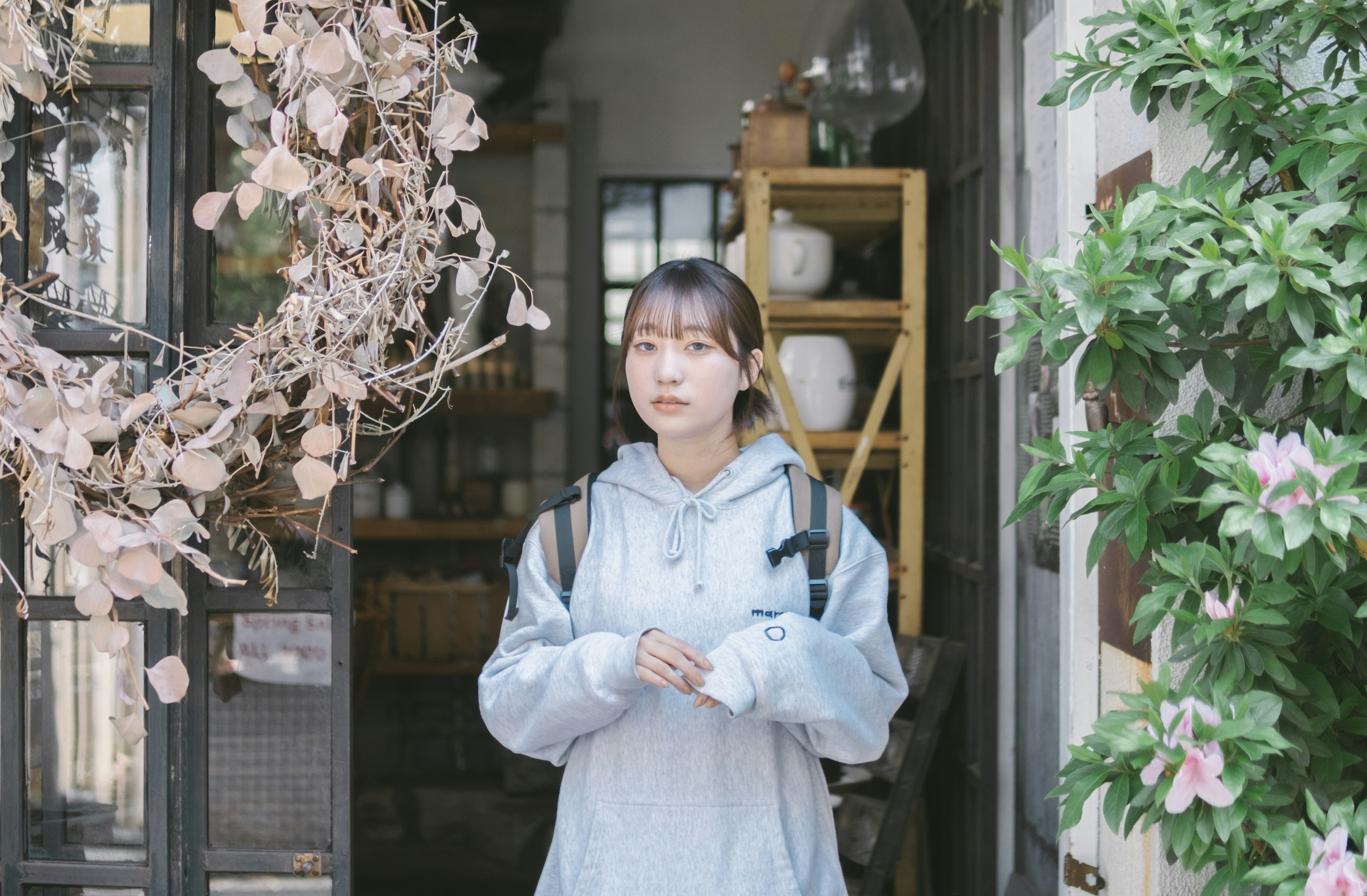 A young woman standing at the door with plants and decorations in the background