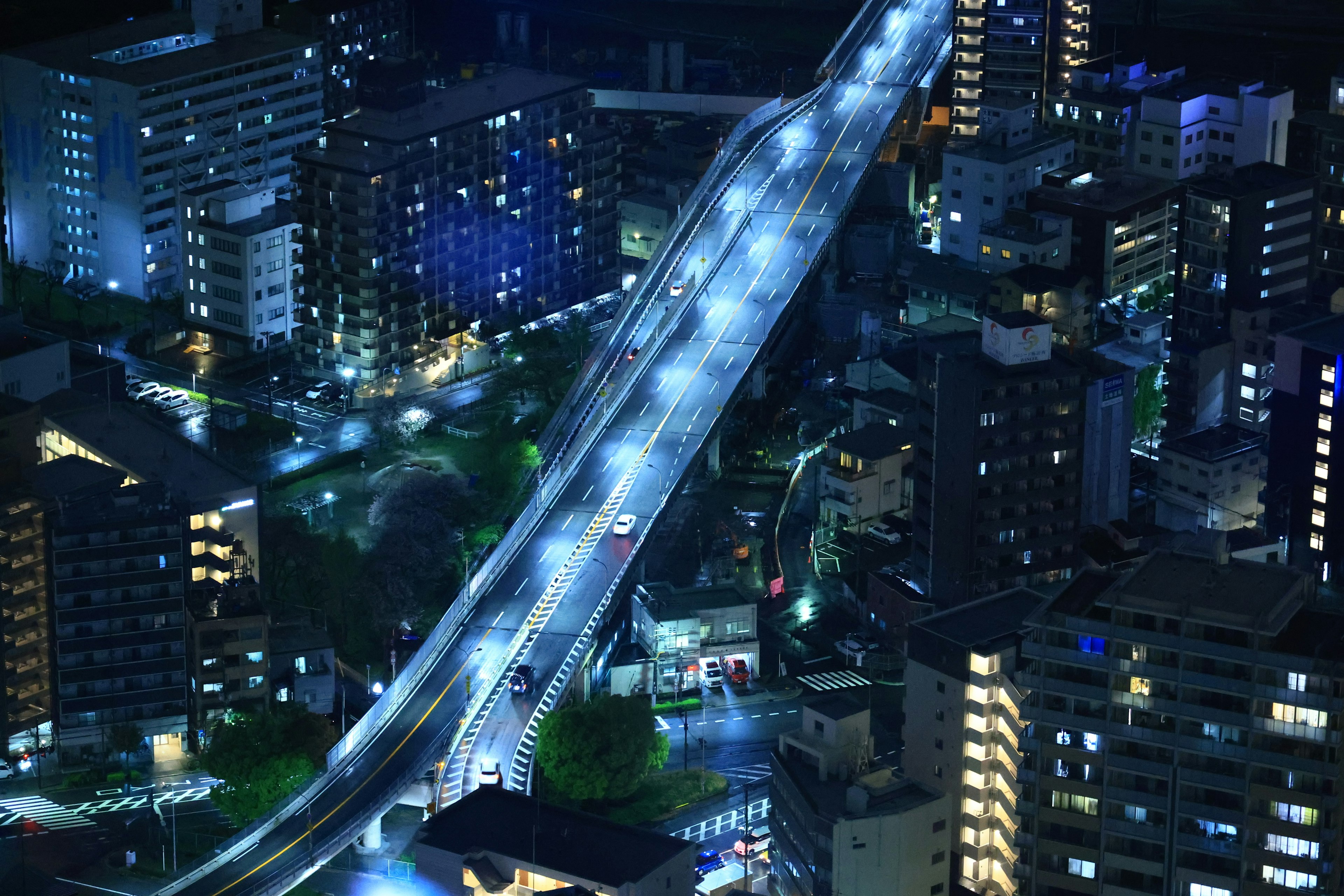 Night cityscape featuring a highway and buildings illuminated by blue lights