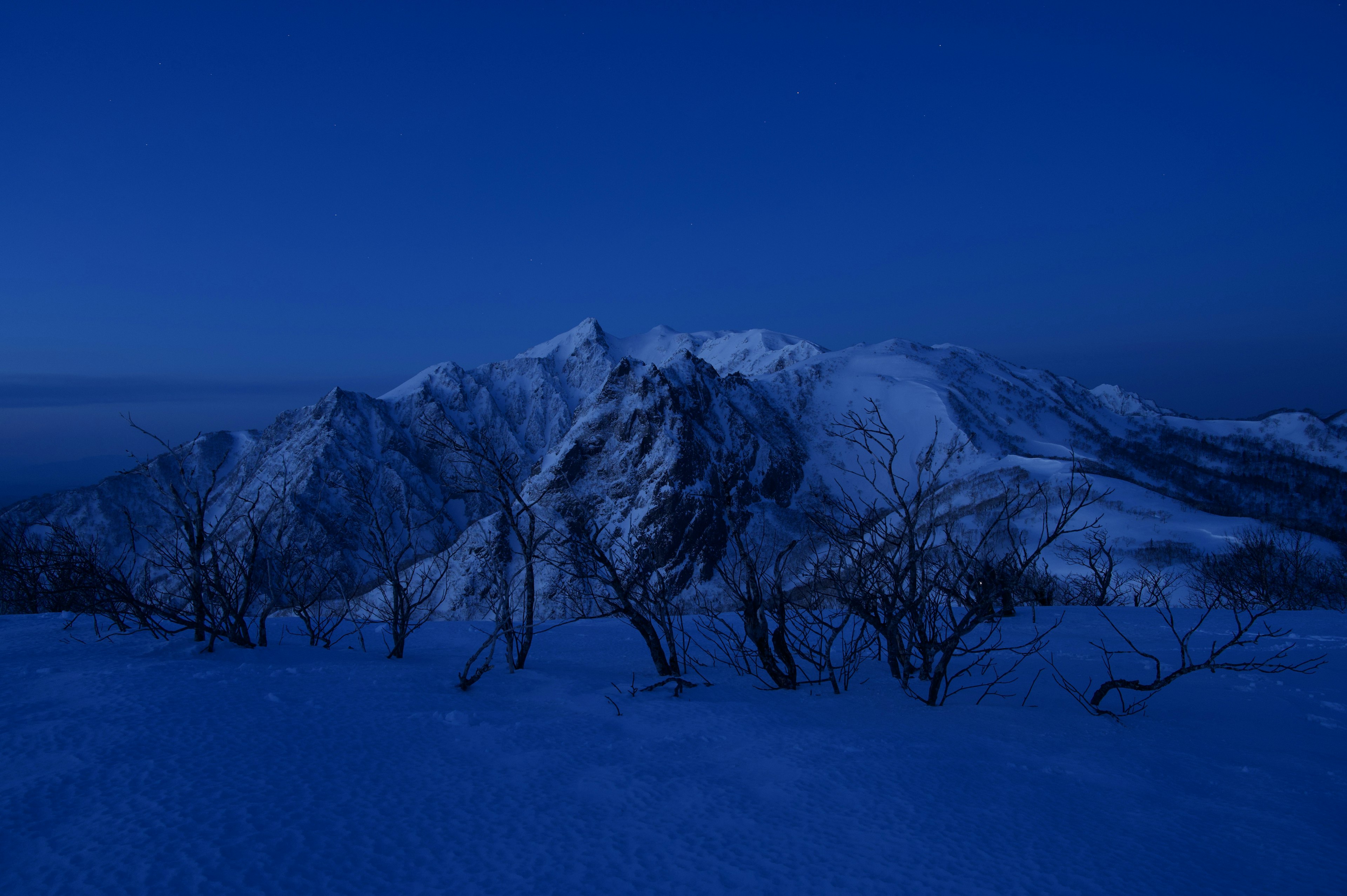 雪に覆われた山々と暗い青の空が広がる風景