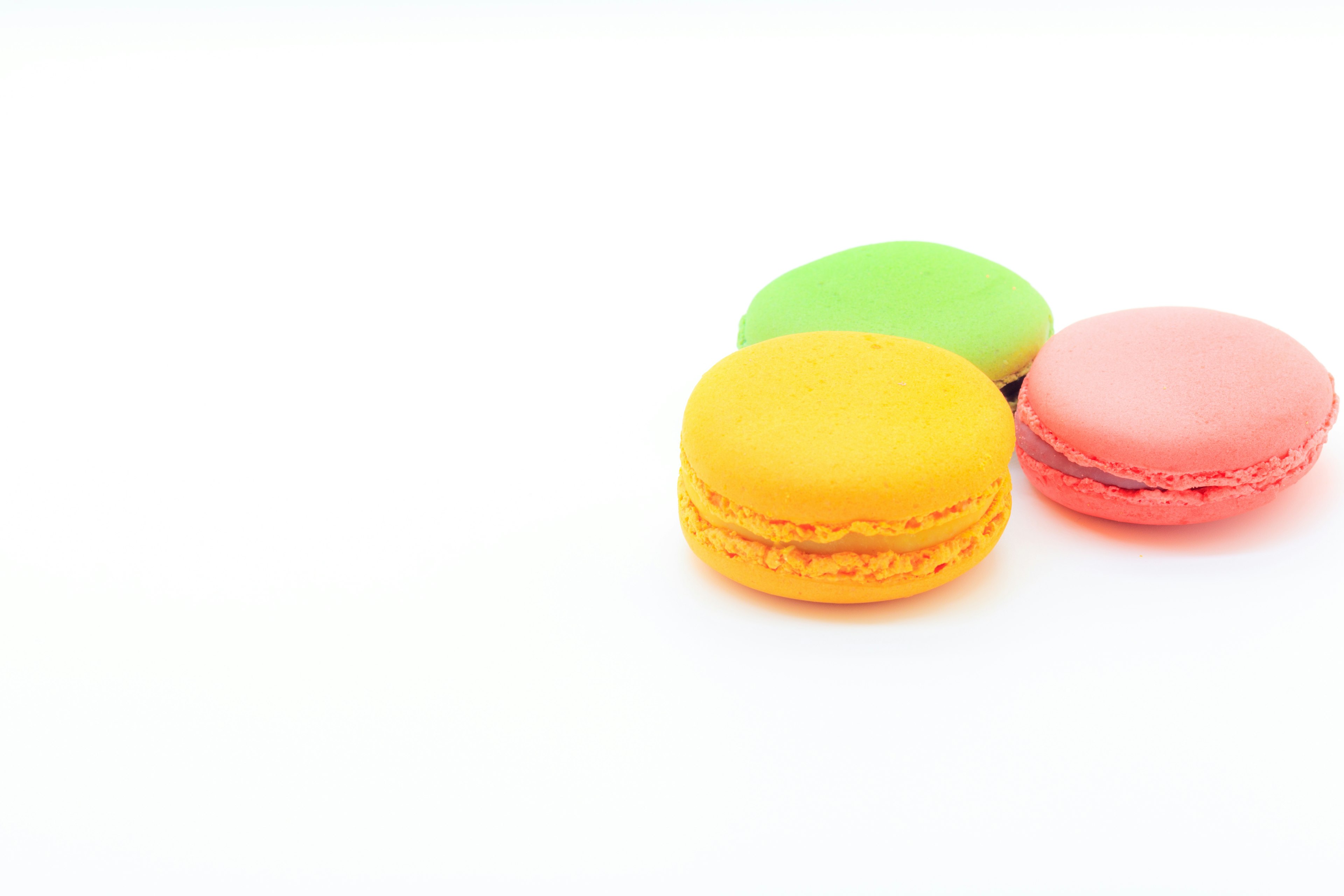 Tiga macarons berwarna kuning hijau dan merah muda di latar belakang putih