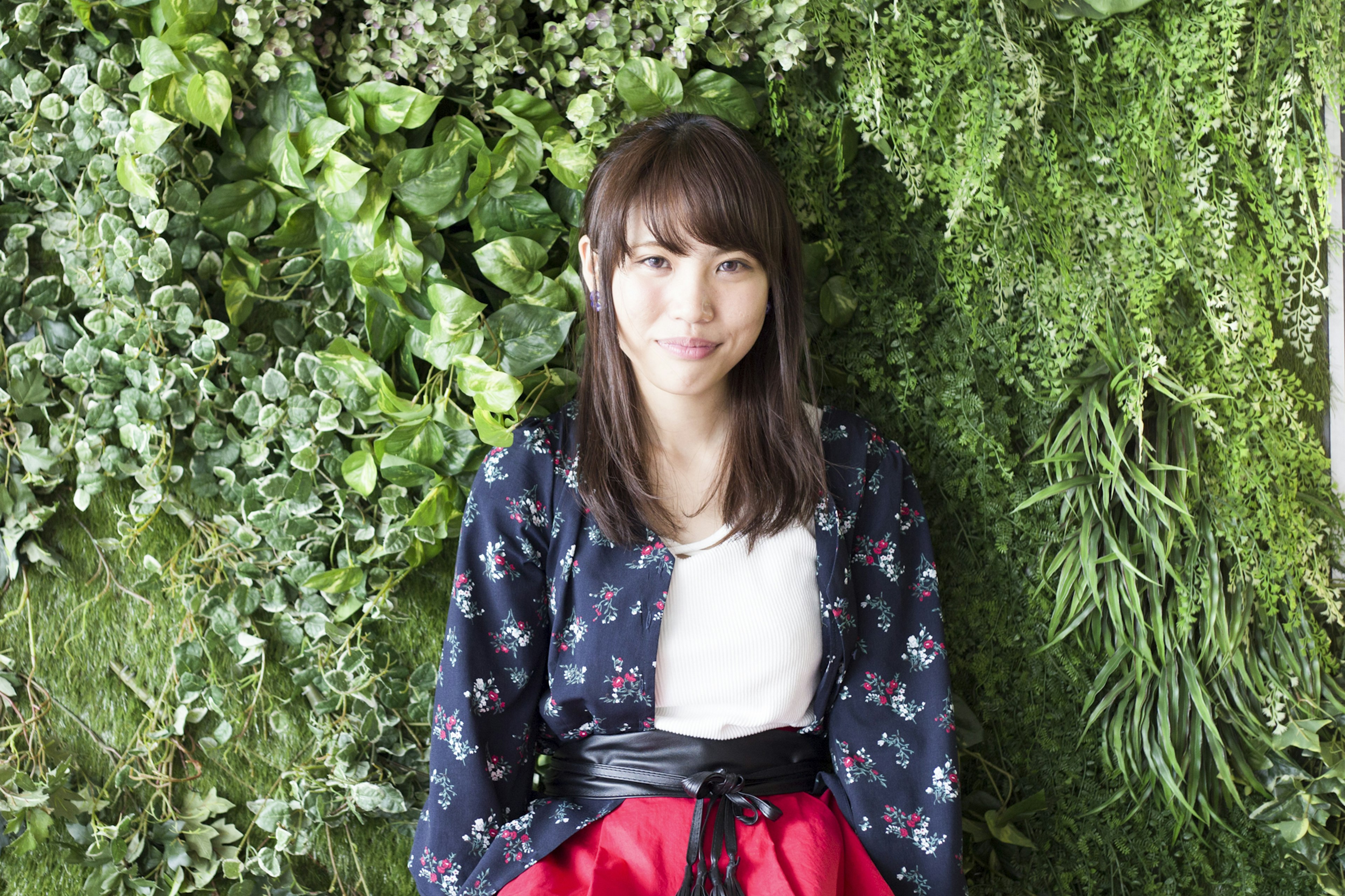 A woman standing in front of a green wall wearing a floral jacket and red skirt