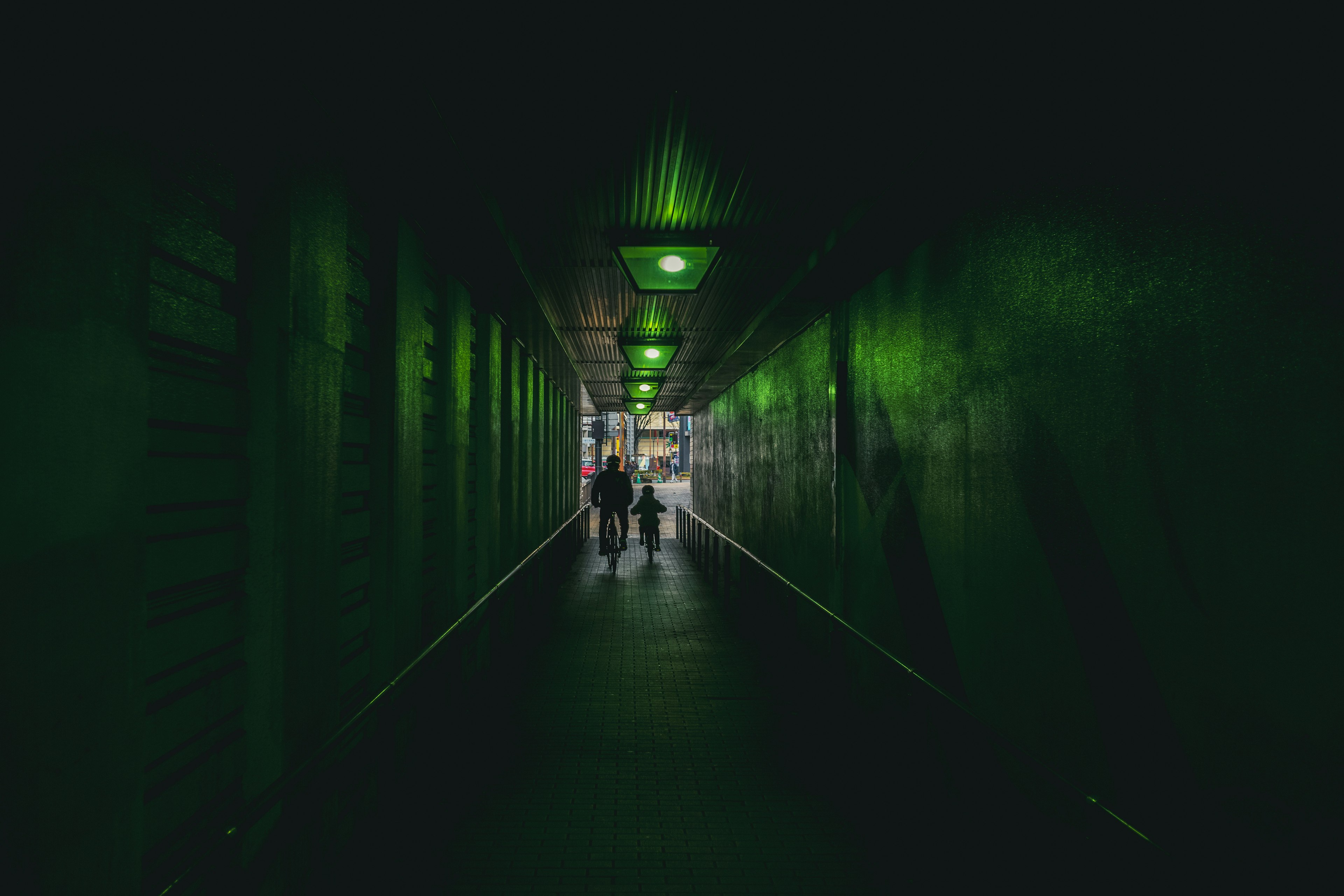 Dark corridor illuminated by green lights with people walking in the distance