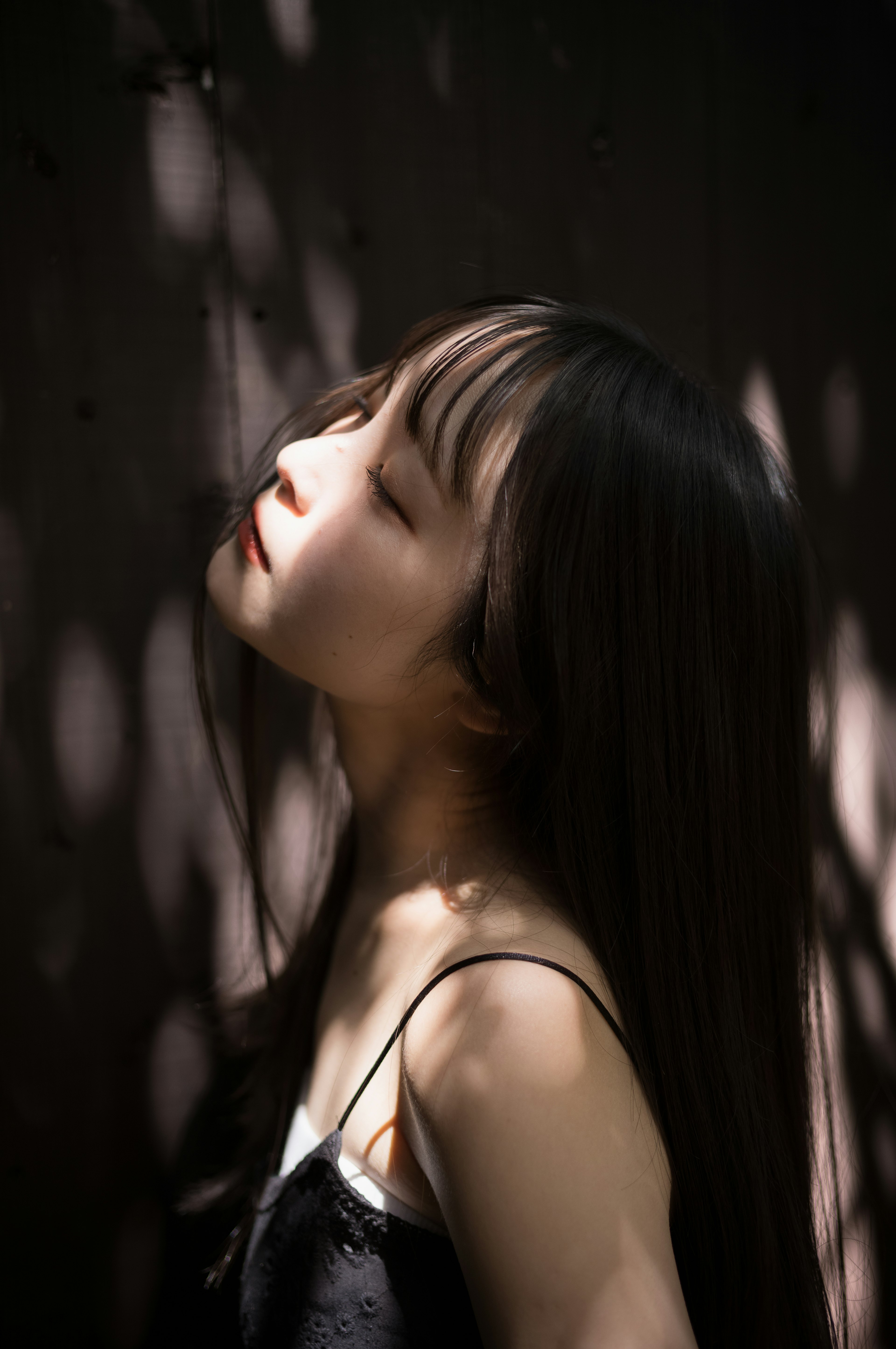 一位长发女性在柔和的光线和阴影中仰望，突显她的特征