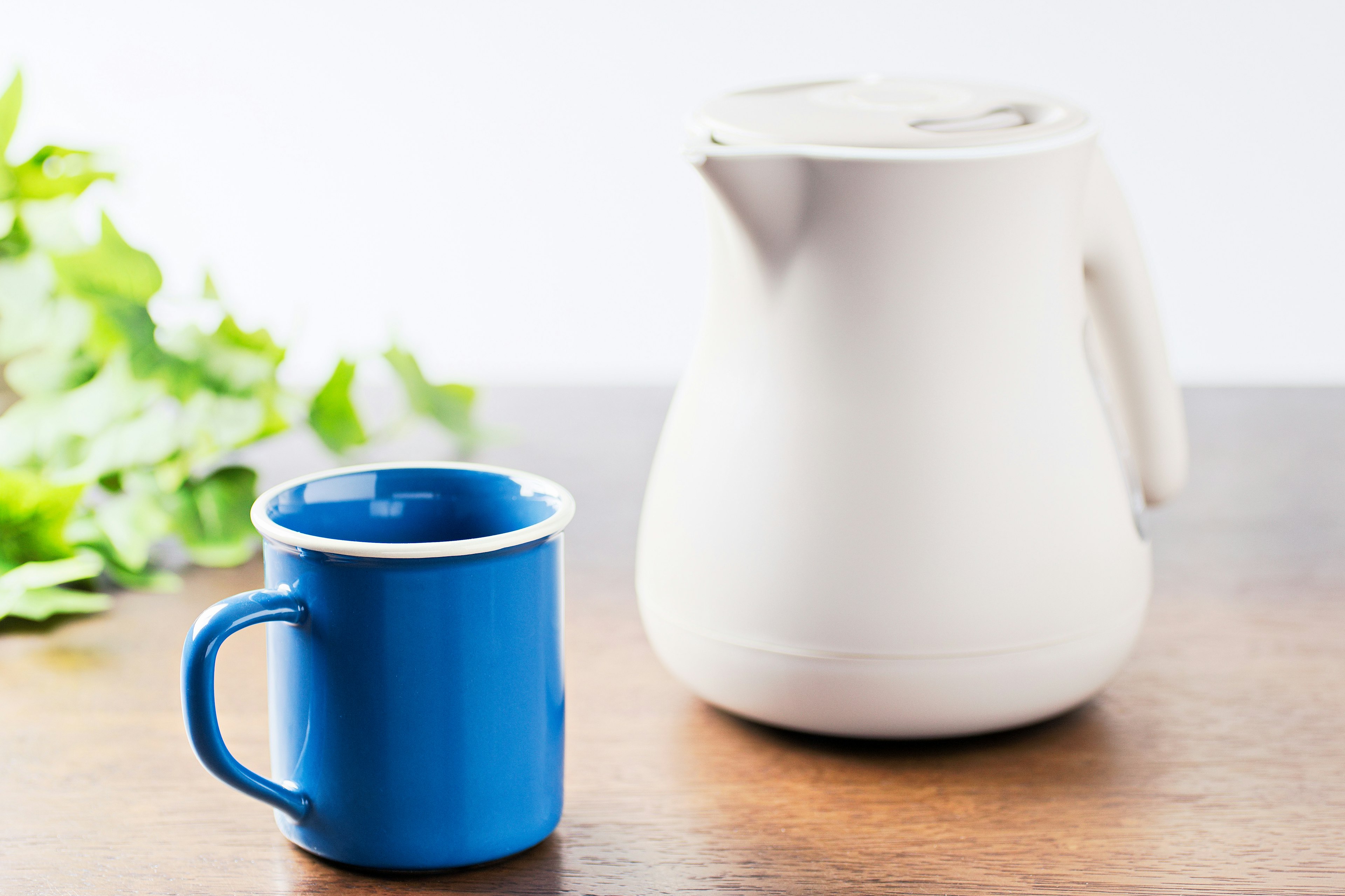 Une bouilloire blanche et une tasse bleue posées sur une table en bois