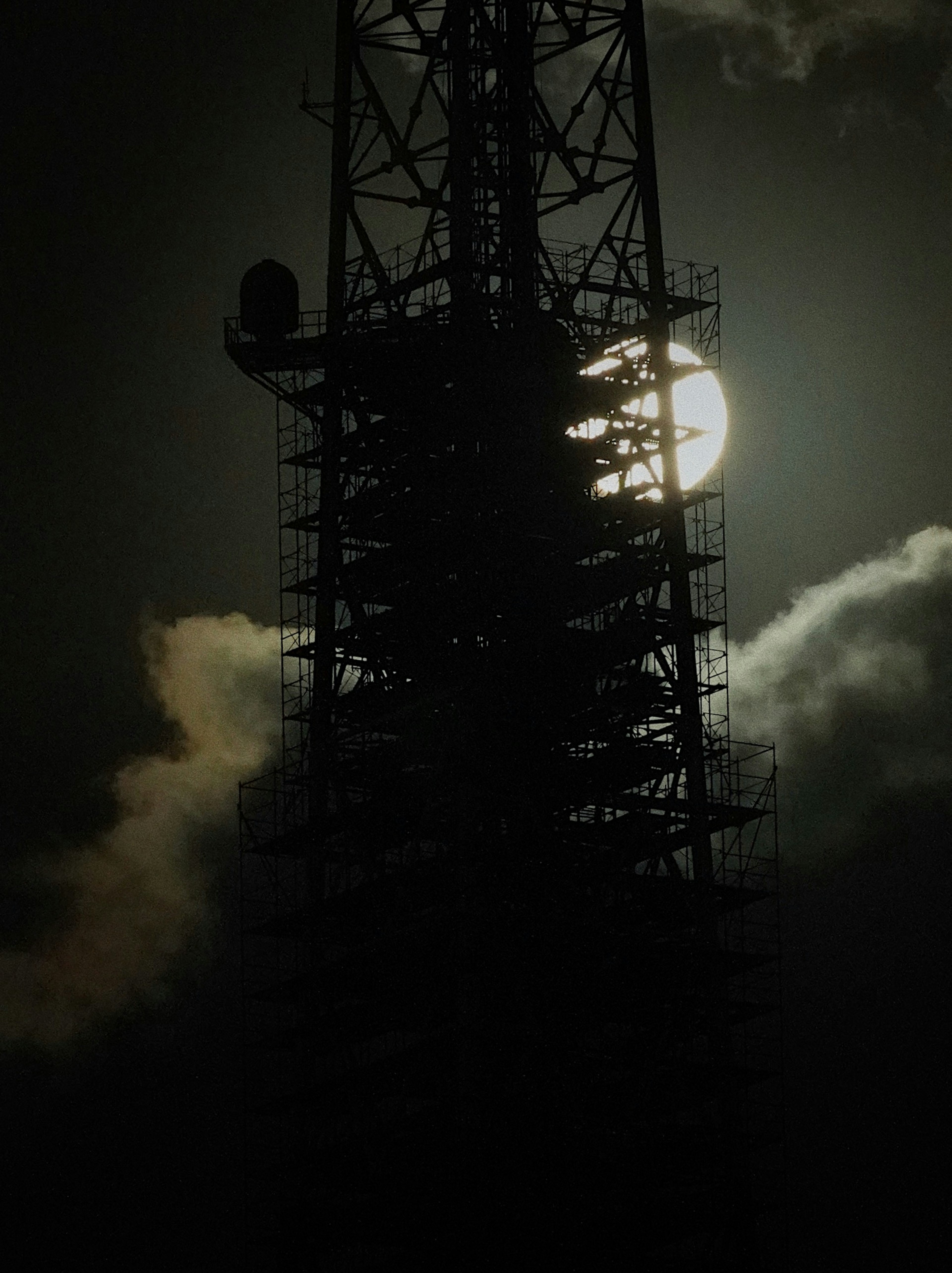 Silhouette di una torre di comunicazione contro il cielo notturno con la luna